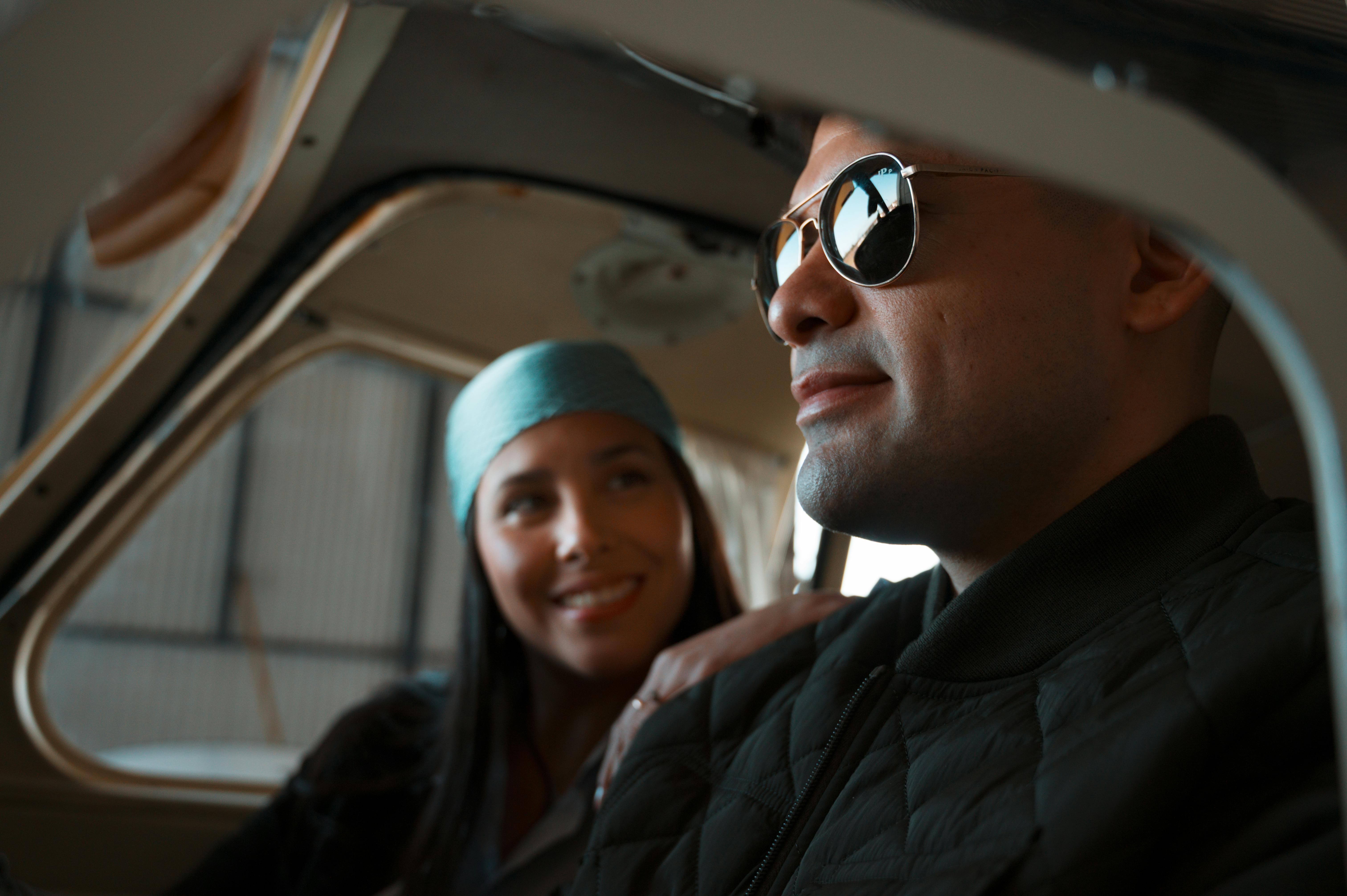 A couple enjoying a moment inside a small aircraft in a hangar setting, with a sense of adventure.