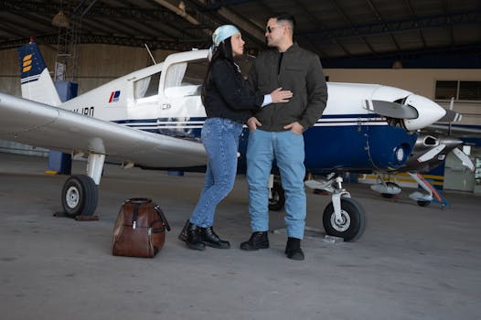 Couple embraces near a small aircraft in an indoor hangar setting, exuding a sense of adventure and travel.