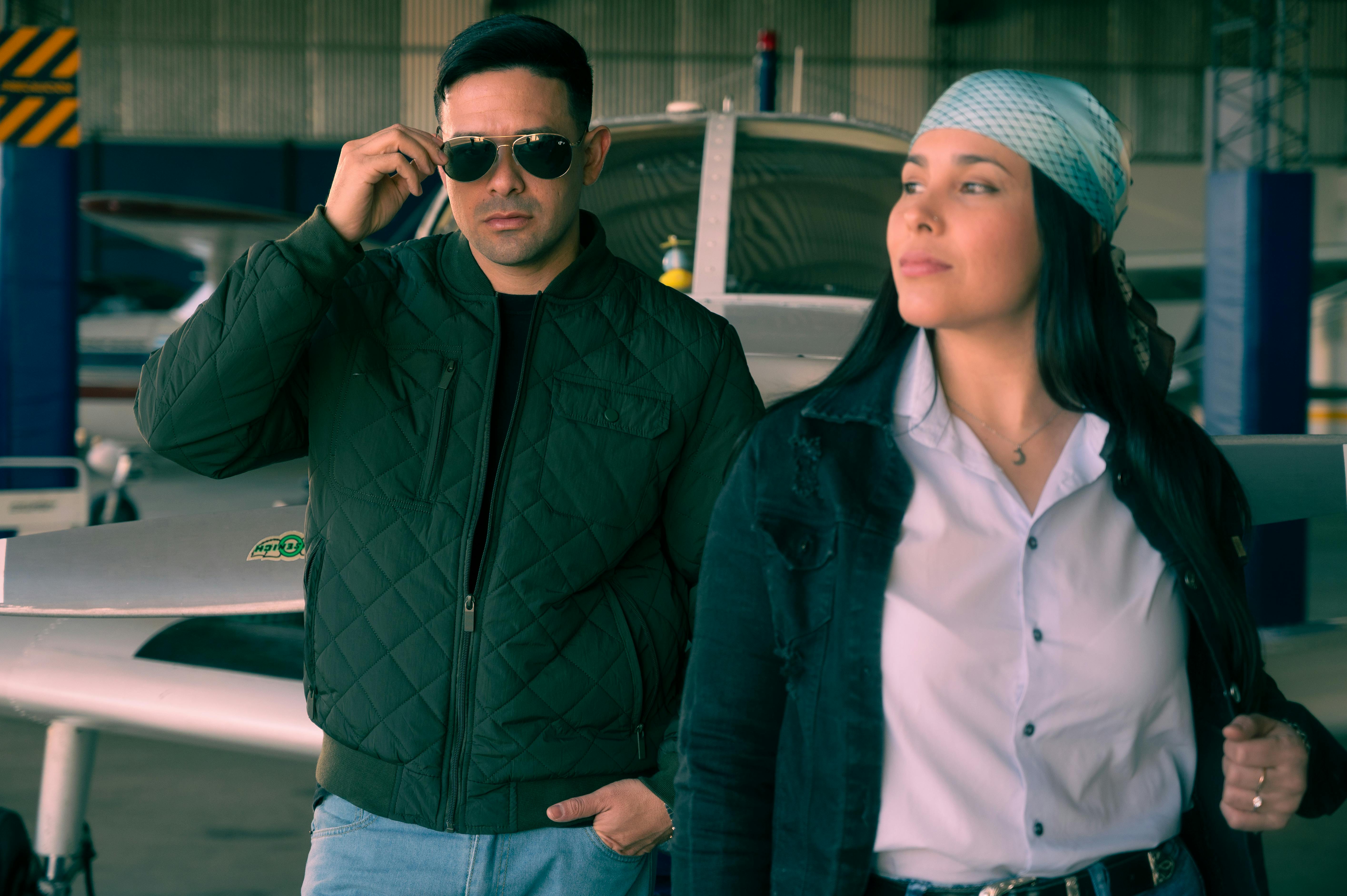 Two stylish individuals in an aircraft hangar, exuding confidence and coolness.