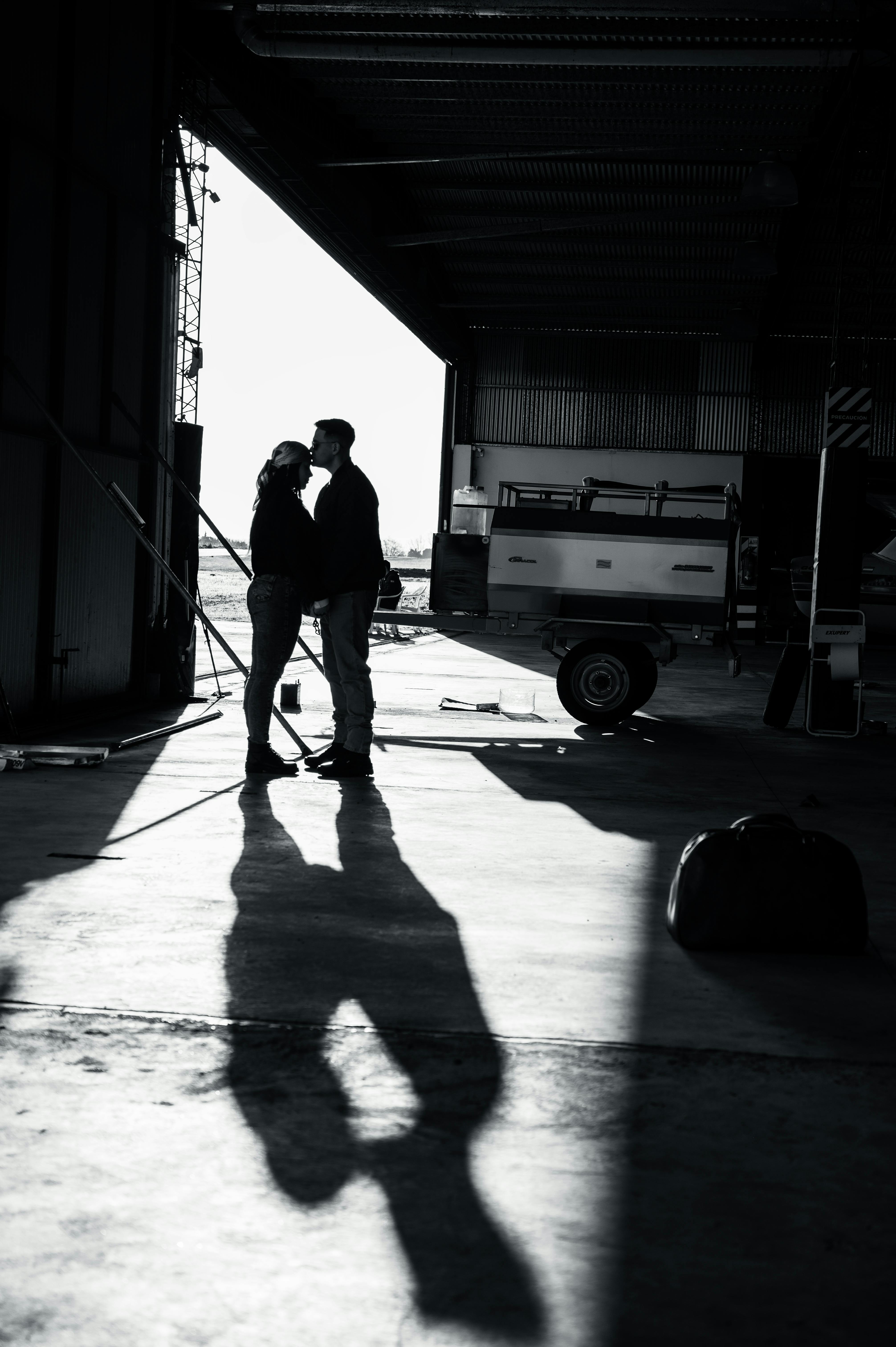 De franc Una parella comparteix un moment en un hangar d'avions amb ombres dramàtiques. Foto d'estoc