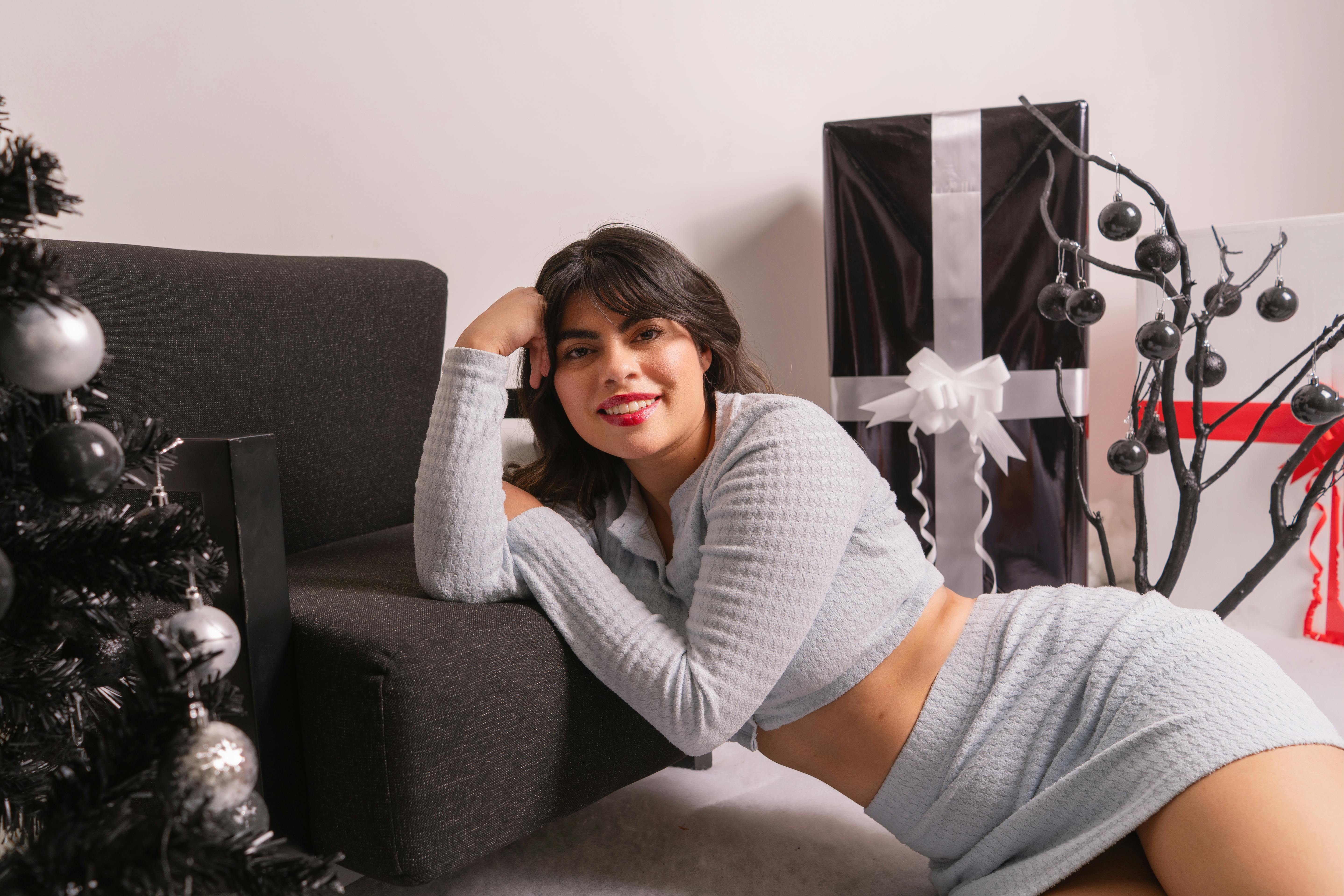 grátis Jovem mulher vestida com roupas de inverno aconchegantes, sentada dentro de casa ao lado de presentes e decorações. Foto profissional