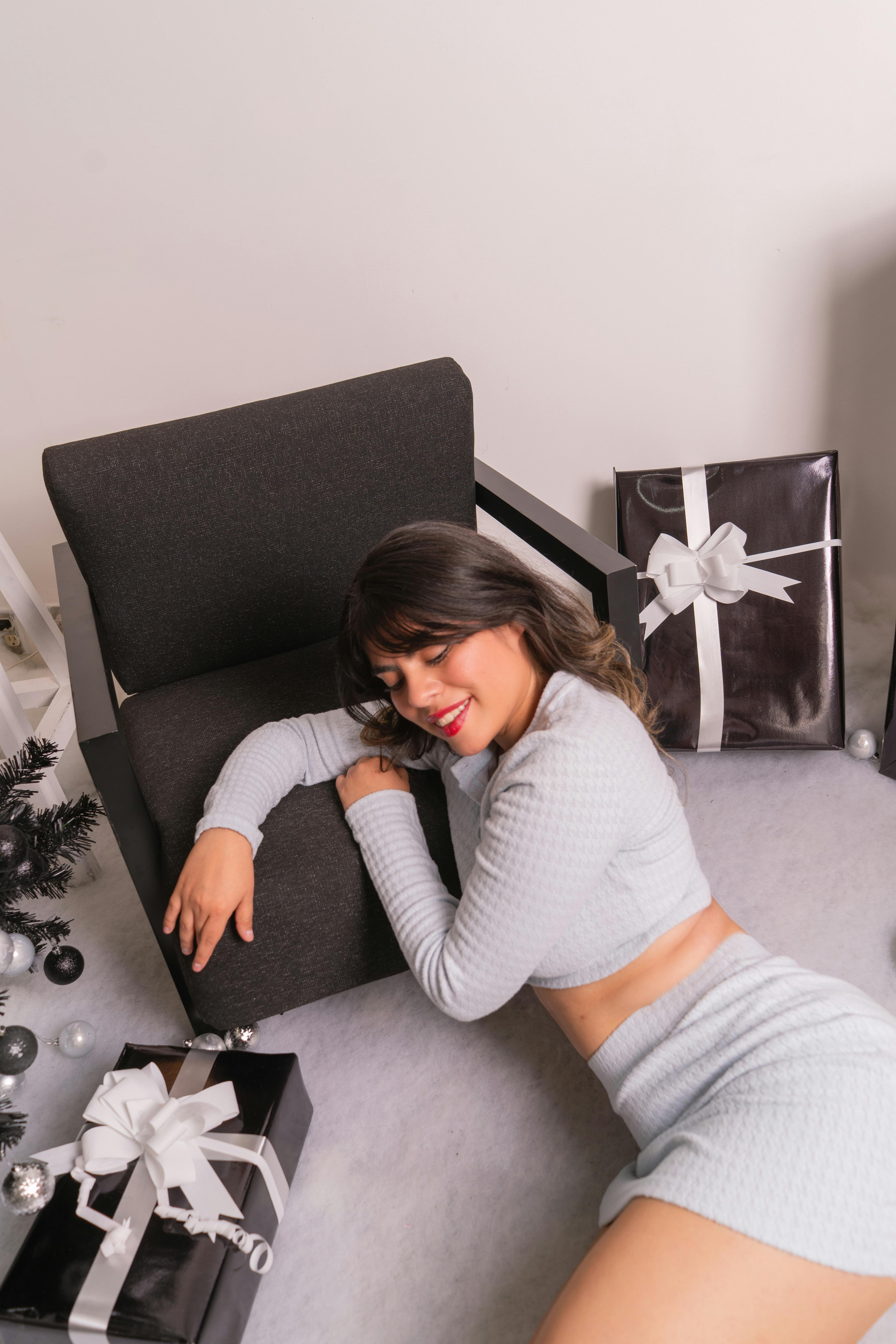 grátis Mulher vestida com roupa de inverno perto de caixas de presentes e uma cadeira, em um ambiente festivo. Foto profissional