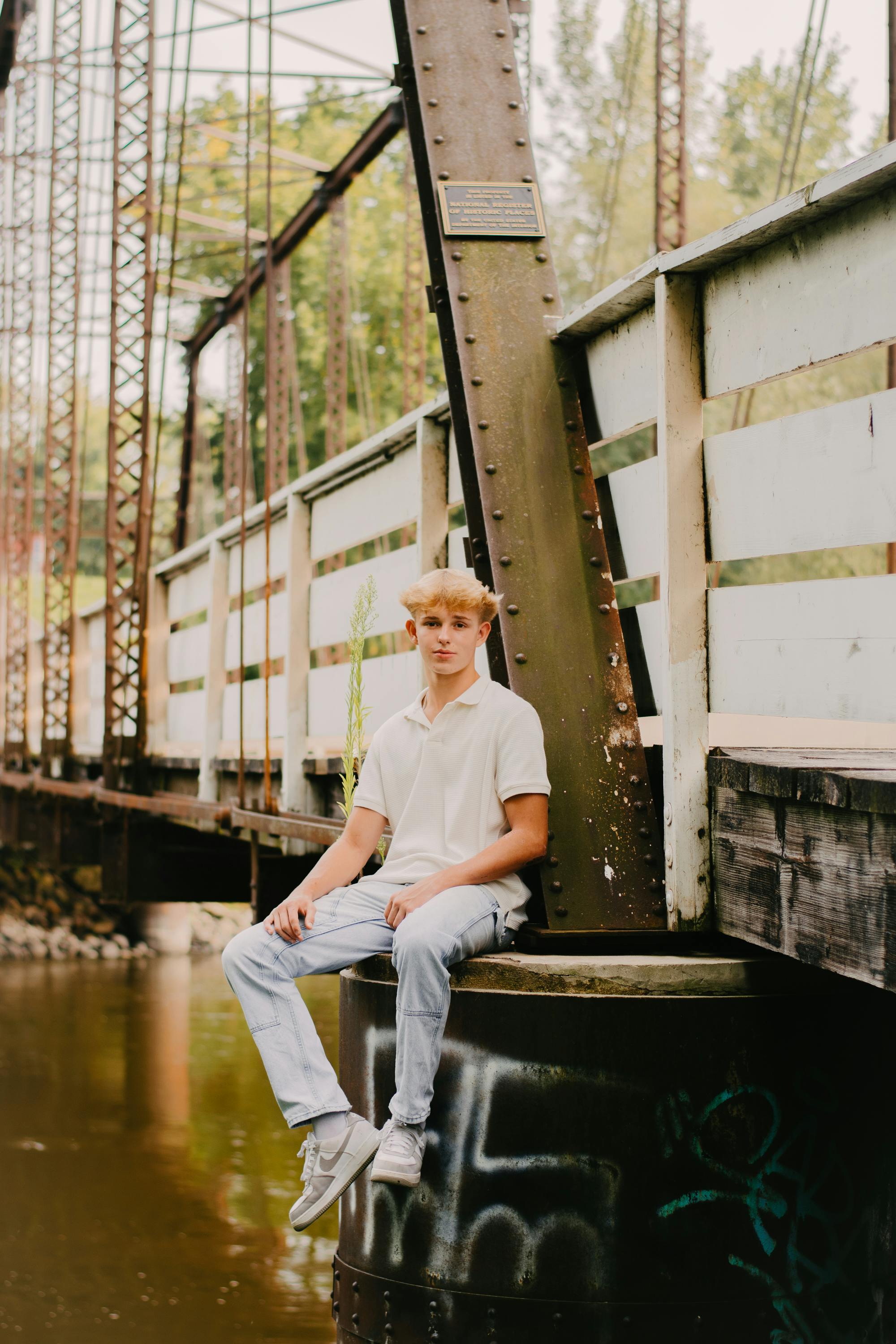 Gratis Hombre joven sentado casualmente en un puente rústico sobre un río, exudando una vibra relajada. Foto de stock