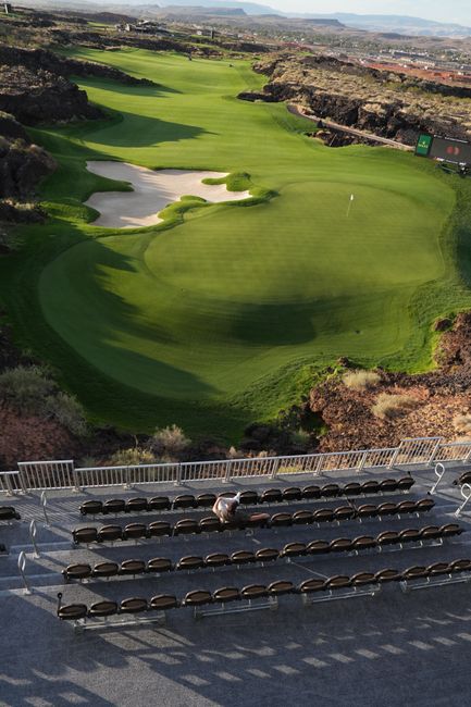 Aerial view of a pristine golf course with empty spectator stands, scenic landscape.