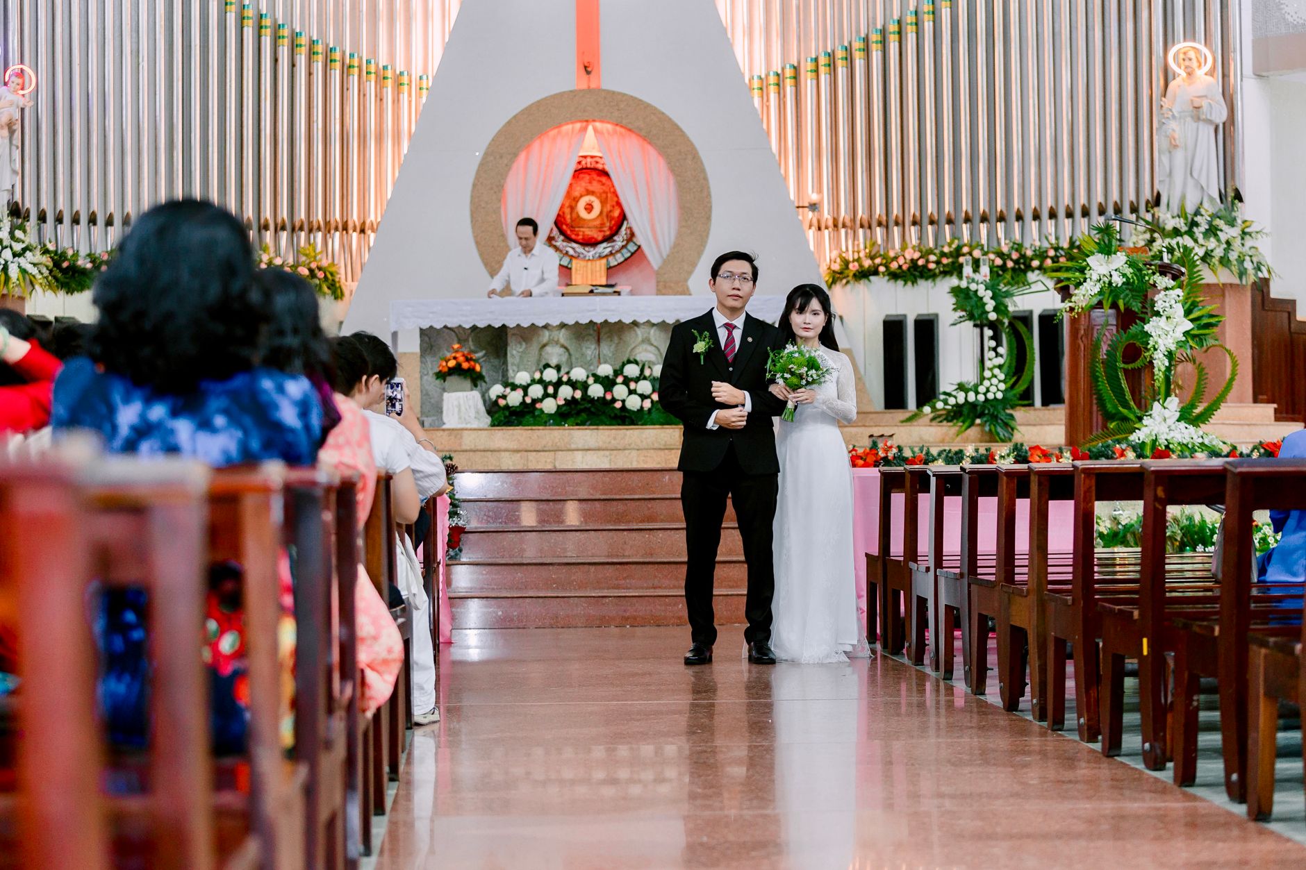 Komitmen Standar Pelayanan dan Dokumentasi Acara Pernikahan Bersama Jagarasa 4 Bride and groom standing in a beautiful church during their wedding ceremony, surrounded by guests and floral decorations.