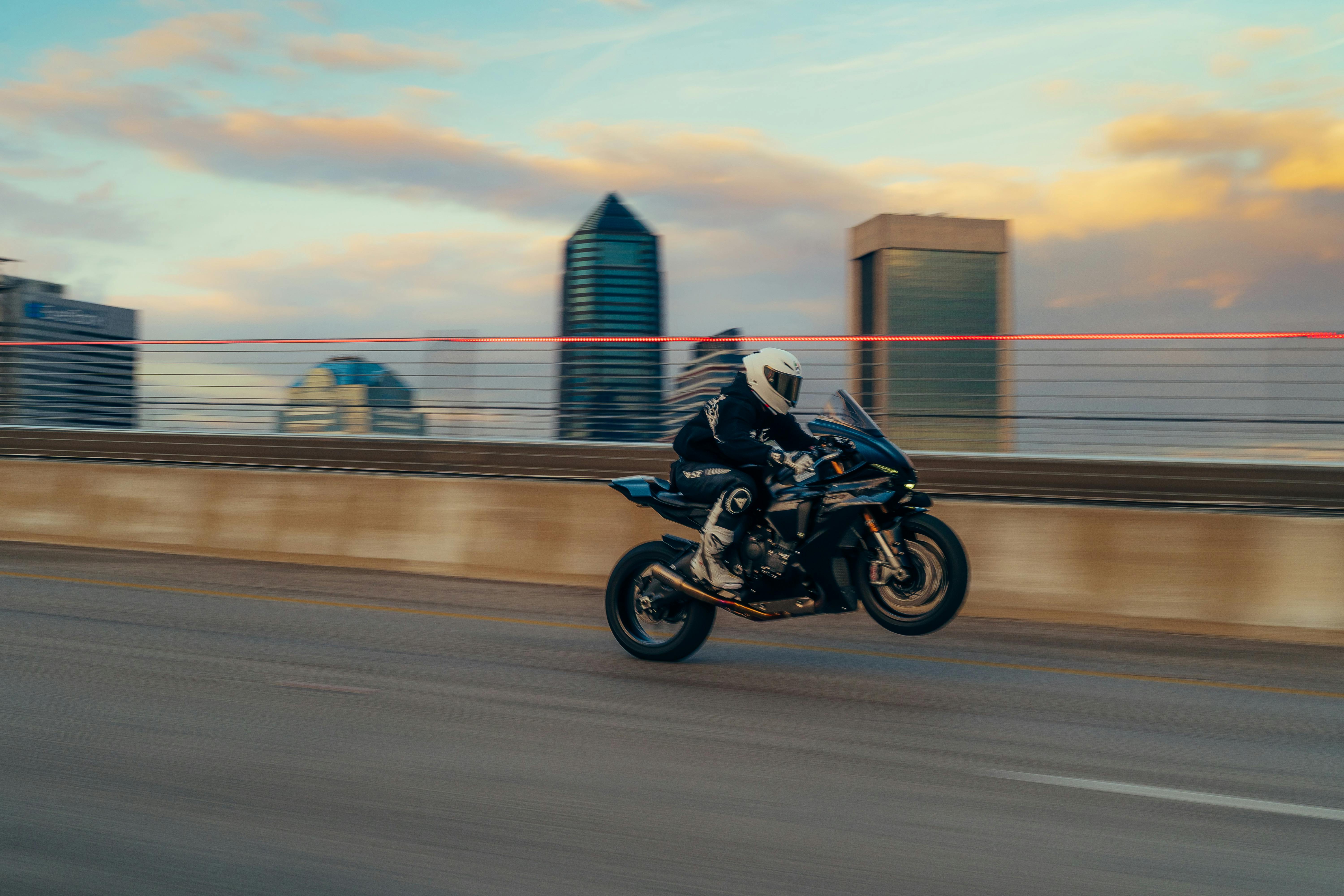 Kostenlos Motorradfahrer in Höchstgeschwindigkeit vor der Kulisse der Stadt bei Sonnenuntergang. Stock-Foto