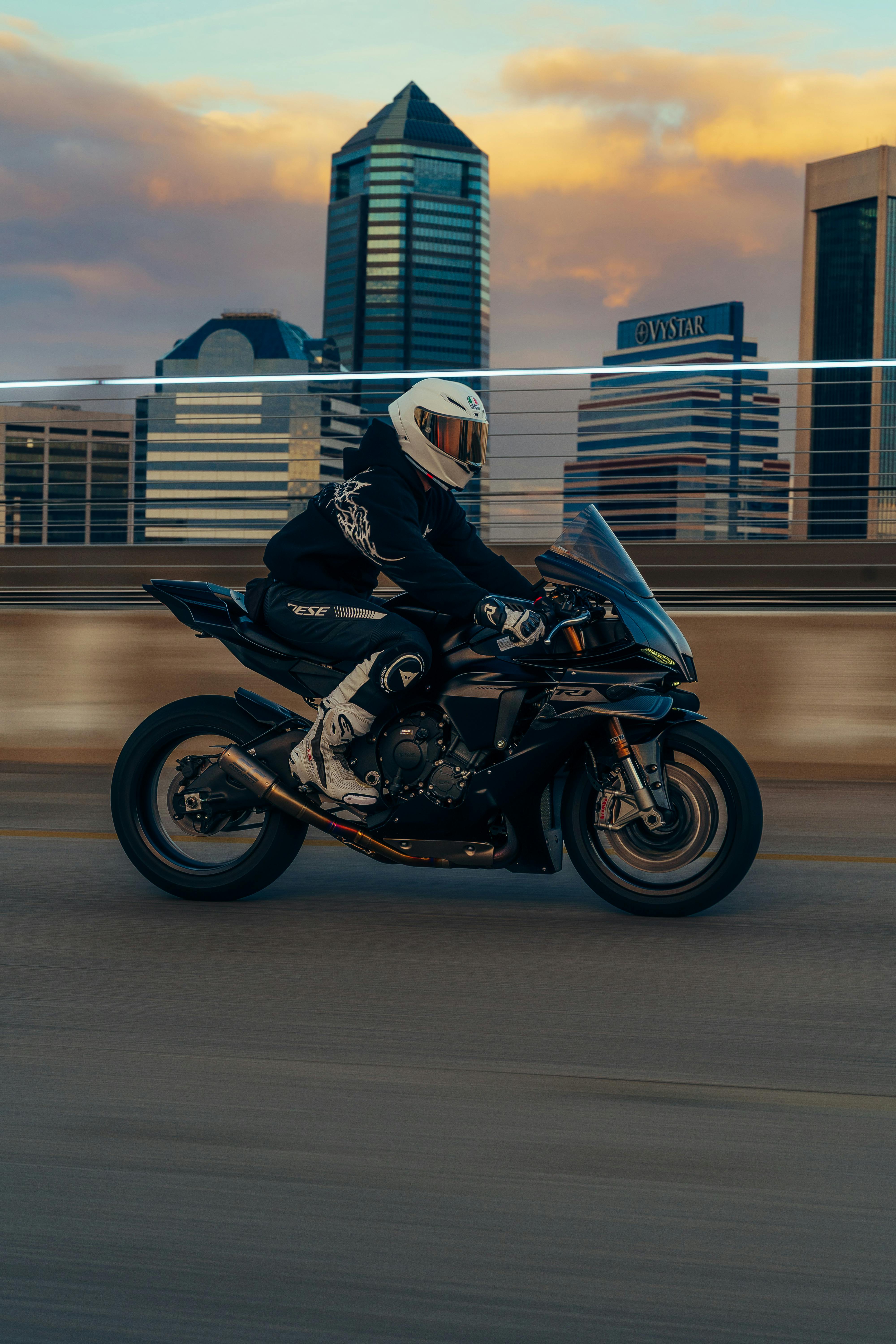 Kostenlos Ein Motorradfahrer fährt bei Sonnenuntergang durch die Straßen der Stadt, die ikonische Skyline ist im Blickfeld. Stock-Foto