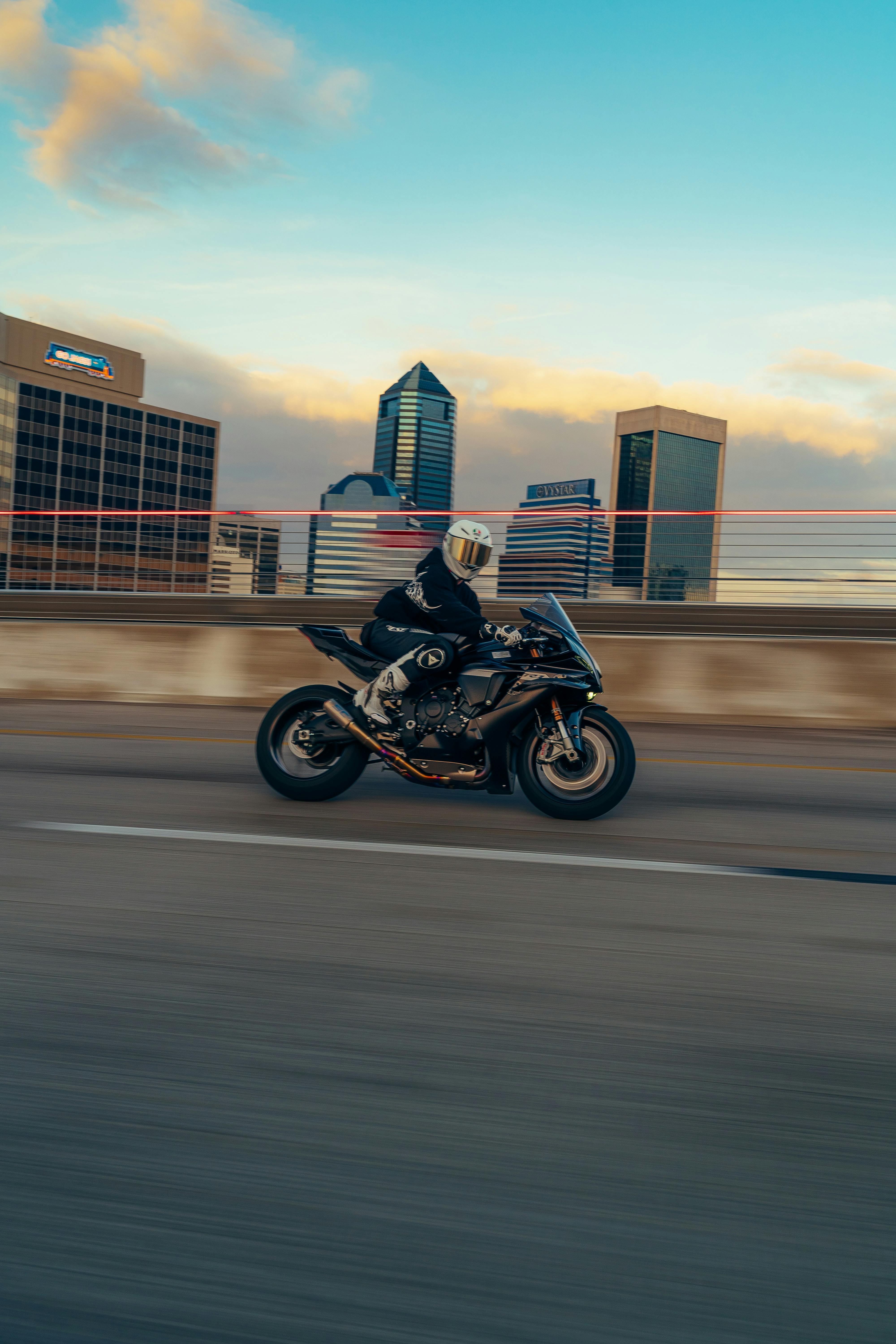 Kostenlos Ein Motorradfahrer rast im Morgengrauen über eine Brücke, im Hintergrund die Skyline der Stadt. Stock-Foto