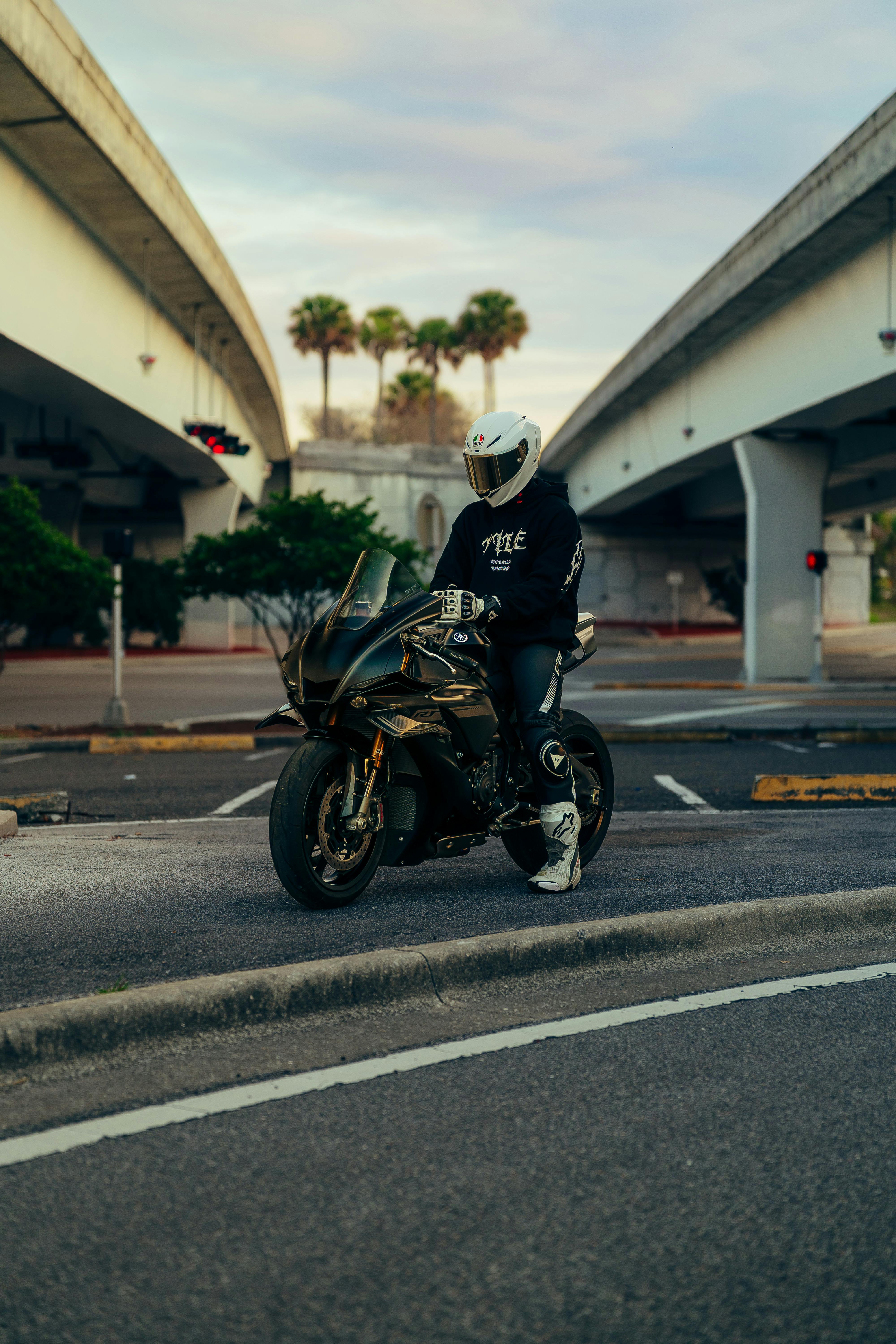 Kostenlos Ein einzelner Motorradfahrer in voller Montur hält in der Dämmerung unter einer Stadtbrücke an. Stock-Foto