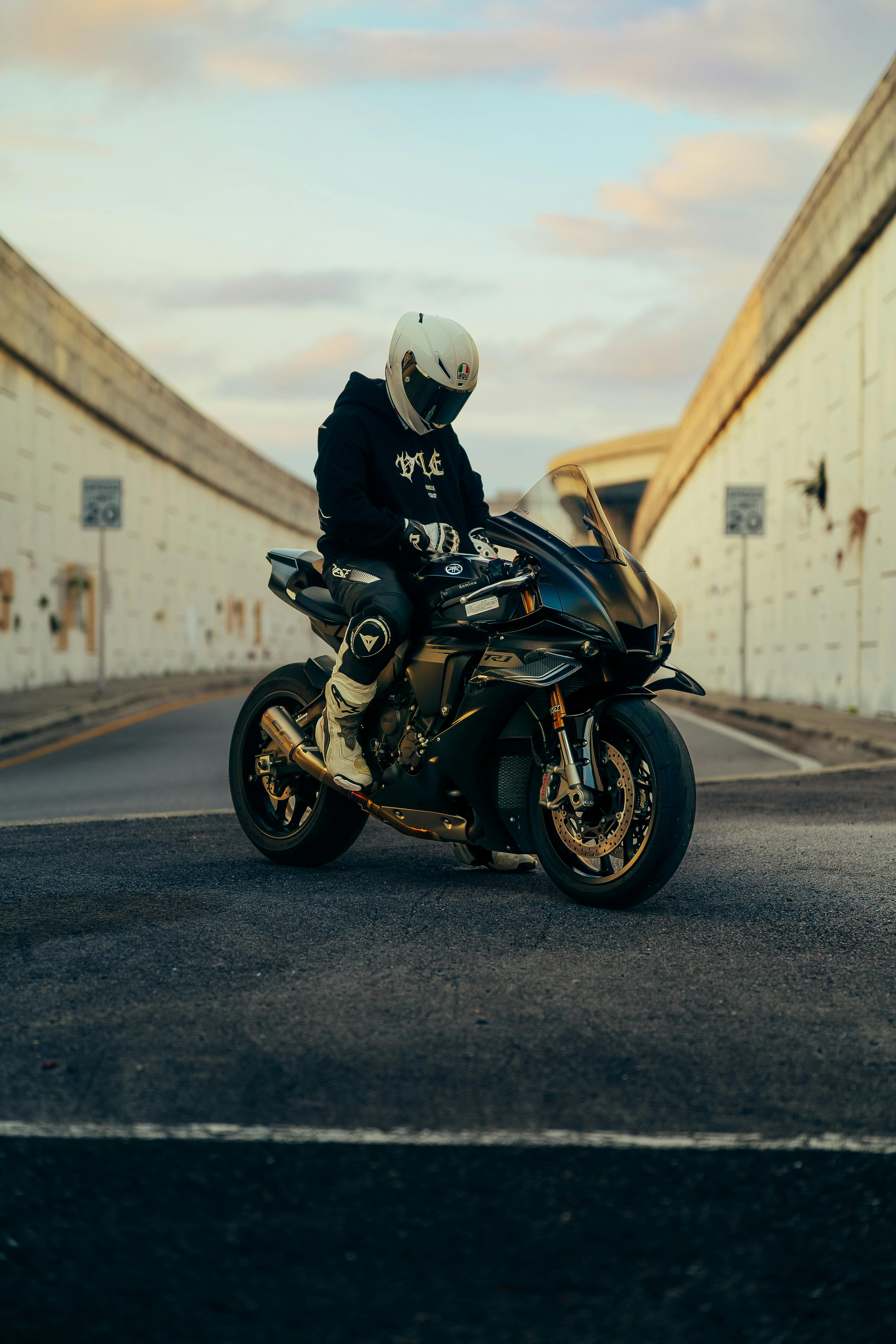 Kostenlos Motorradfahrer mit Helm posiert in der Dämmerung mit seinem Sportmotorrad in einer städtischen Gasse. Stock-Foto