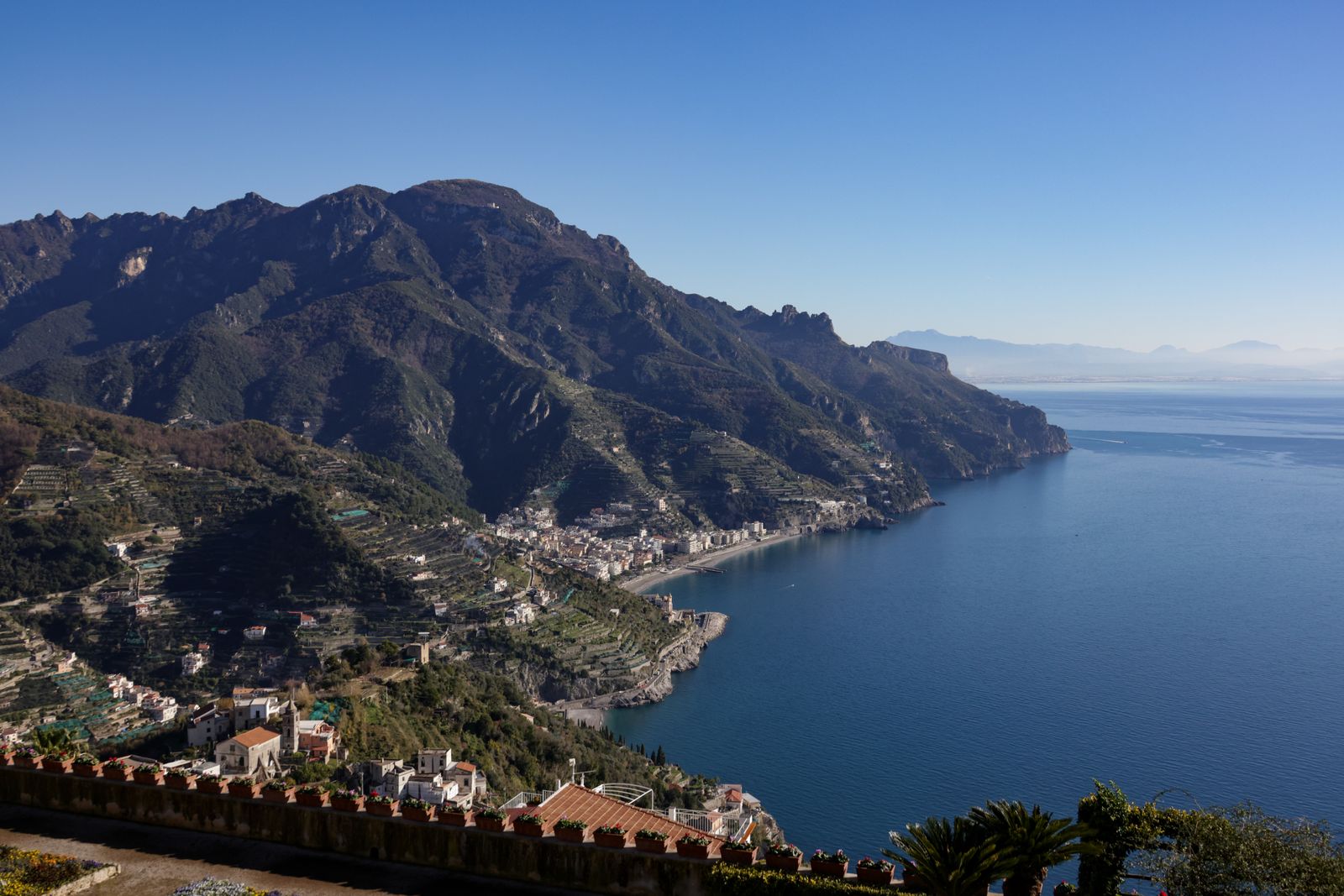 The mountains and terraced hillsides of the Amalfi Coast dropping to a deep blue bay, seen from a high viewpoint on the Path of the Gods in Italy