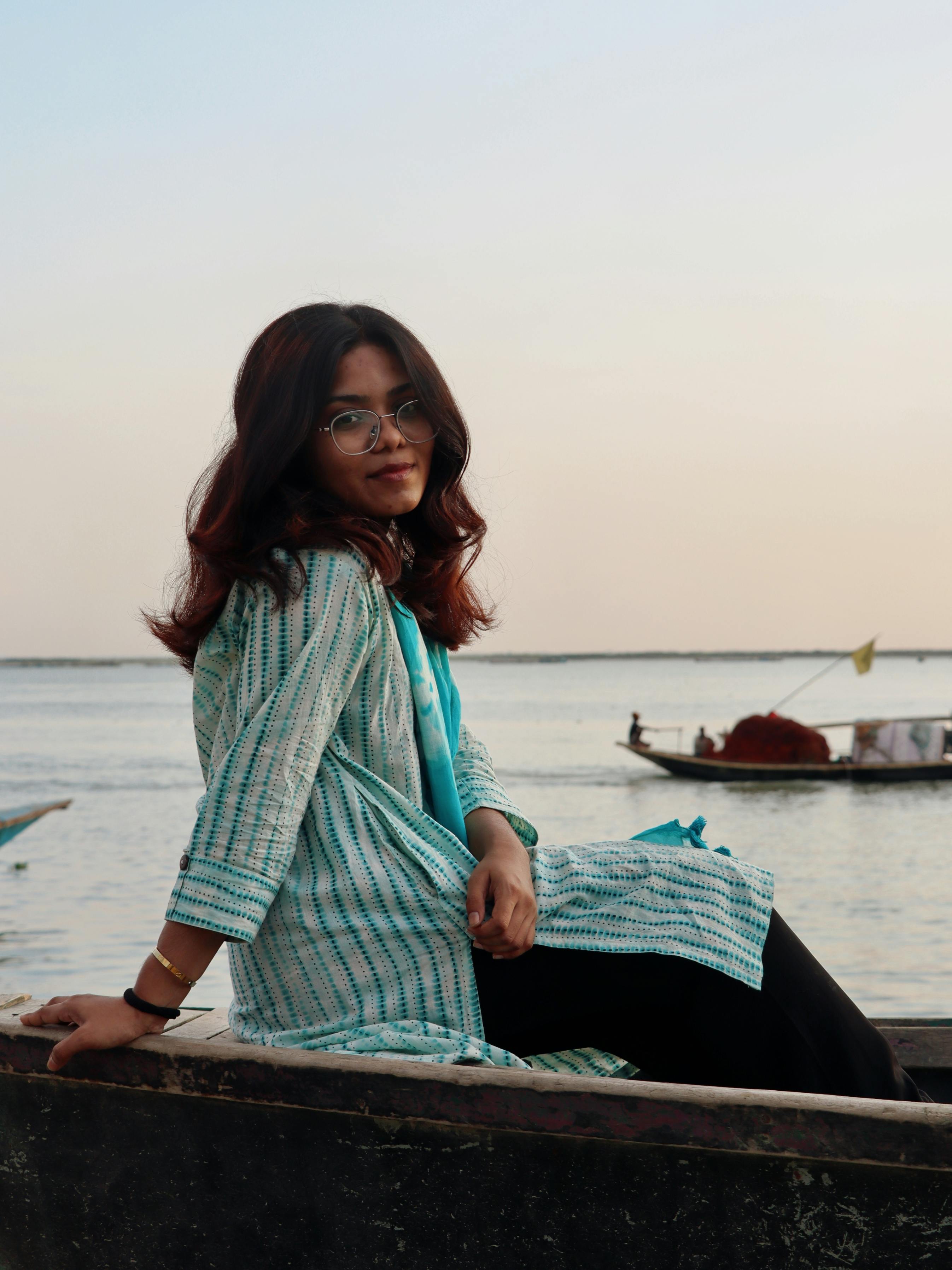 Gratis Una escena serena de una mujer joven sentada a la orilla del río durante la puesta de sol, reflejando tranquilidad. Foto de stock