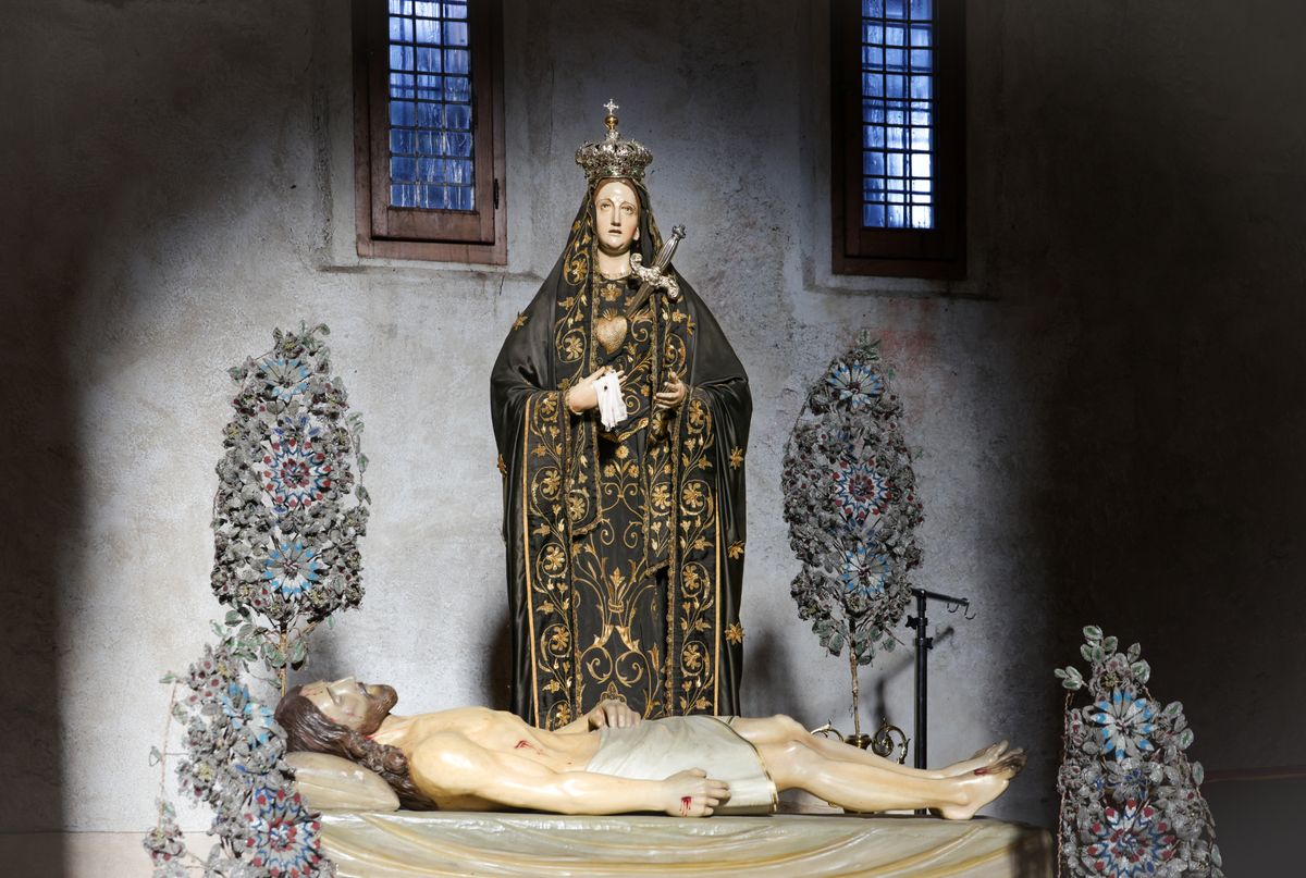 Statuie intr-o capela intunecata, cu pereti acoperiti de daruri votive