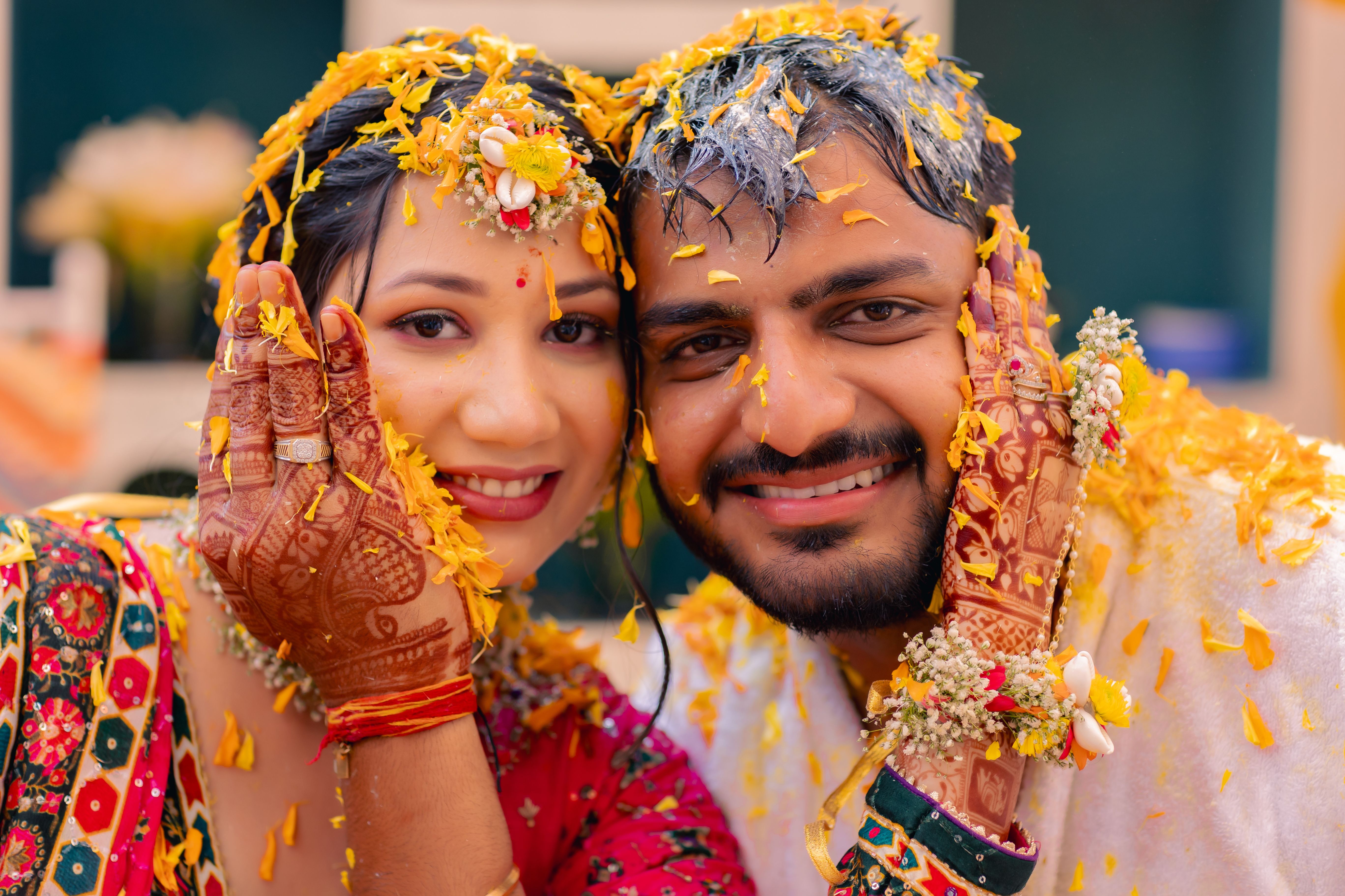 Smiling couple in traditional Indian attire celebrating a ceremonial pre-wedding ritual adorned with flower petals.