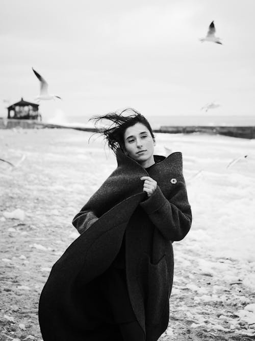 Free Woman Wearing Black Coat Standing on Beach Stock Photo