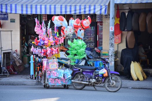 Colorful street vendor motorcycle displaying toys and balloons on an urban street scene.