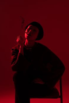 Silhouette of a woman sitting and smoking in dramatic red light.