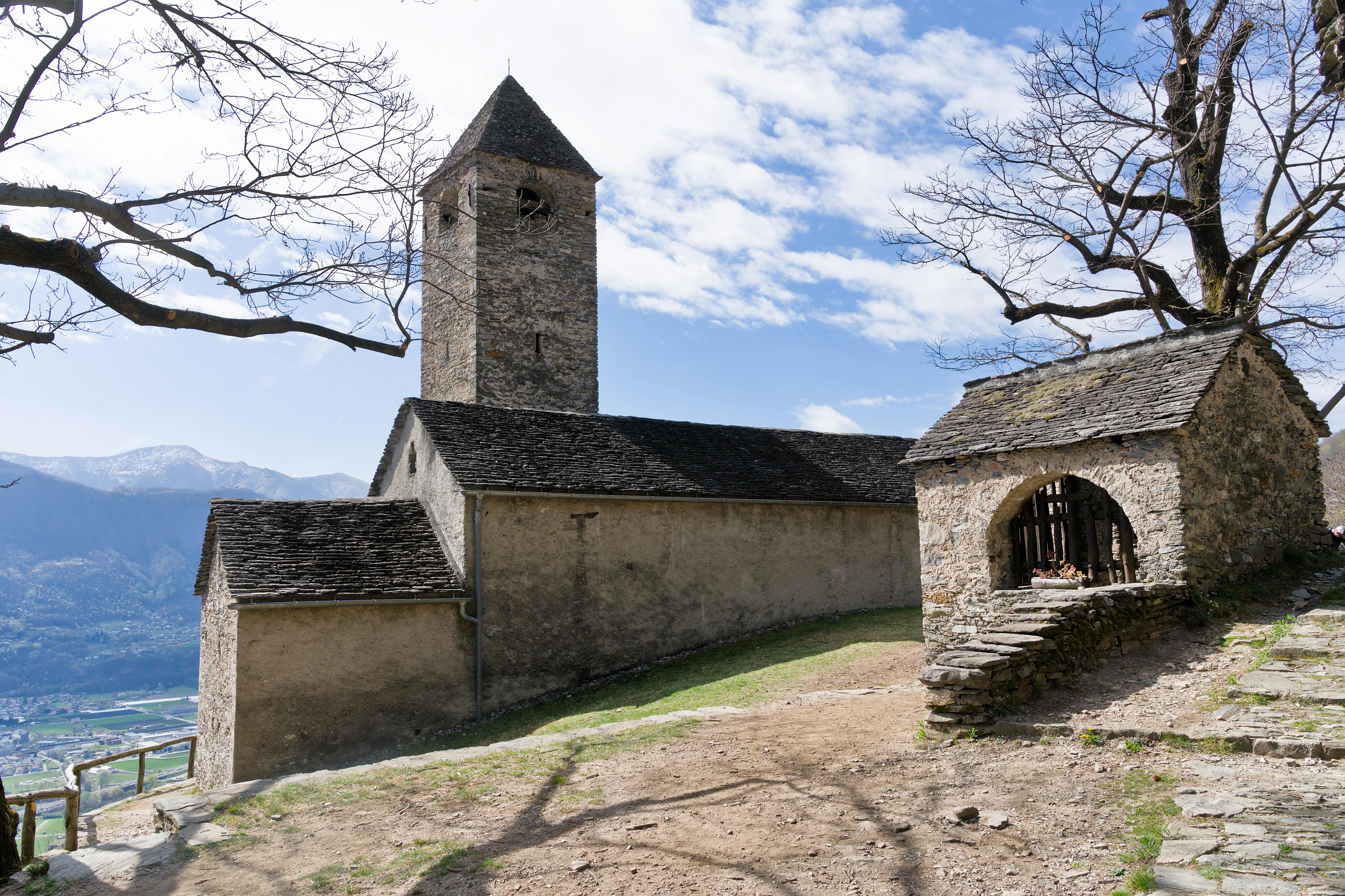 A charming stone church with bell tower in a scenic Swiss village, framed by bare trees.