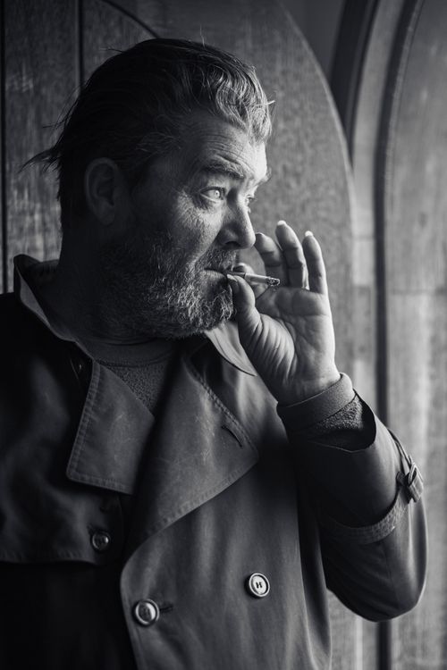 Free Moody black and white portrait of a man smoking in an archway, capturing dramatic light and shadow. Stock Photo