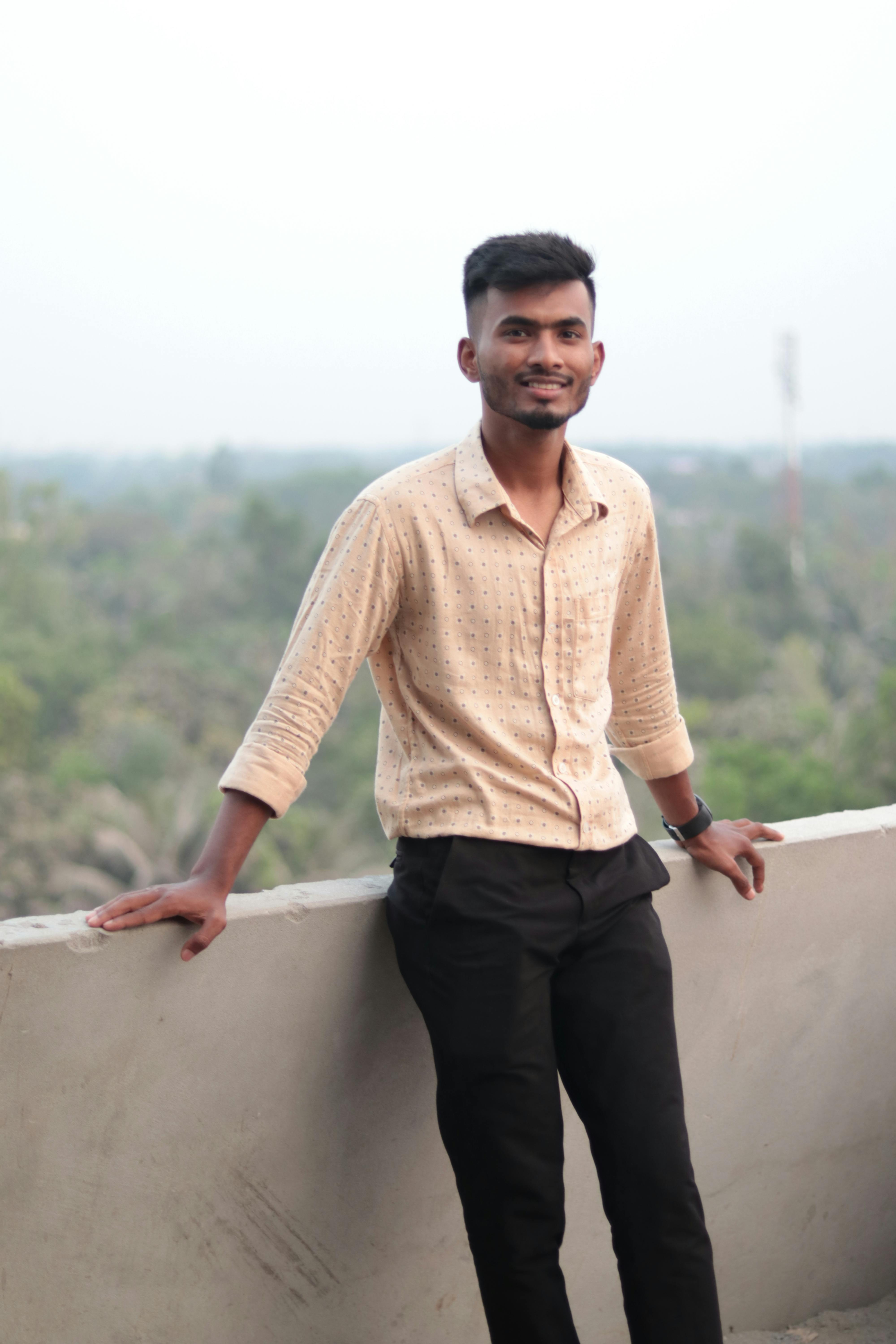 Portrait of a young man standing on a balcony with a scenic outdoor view.