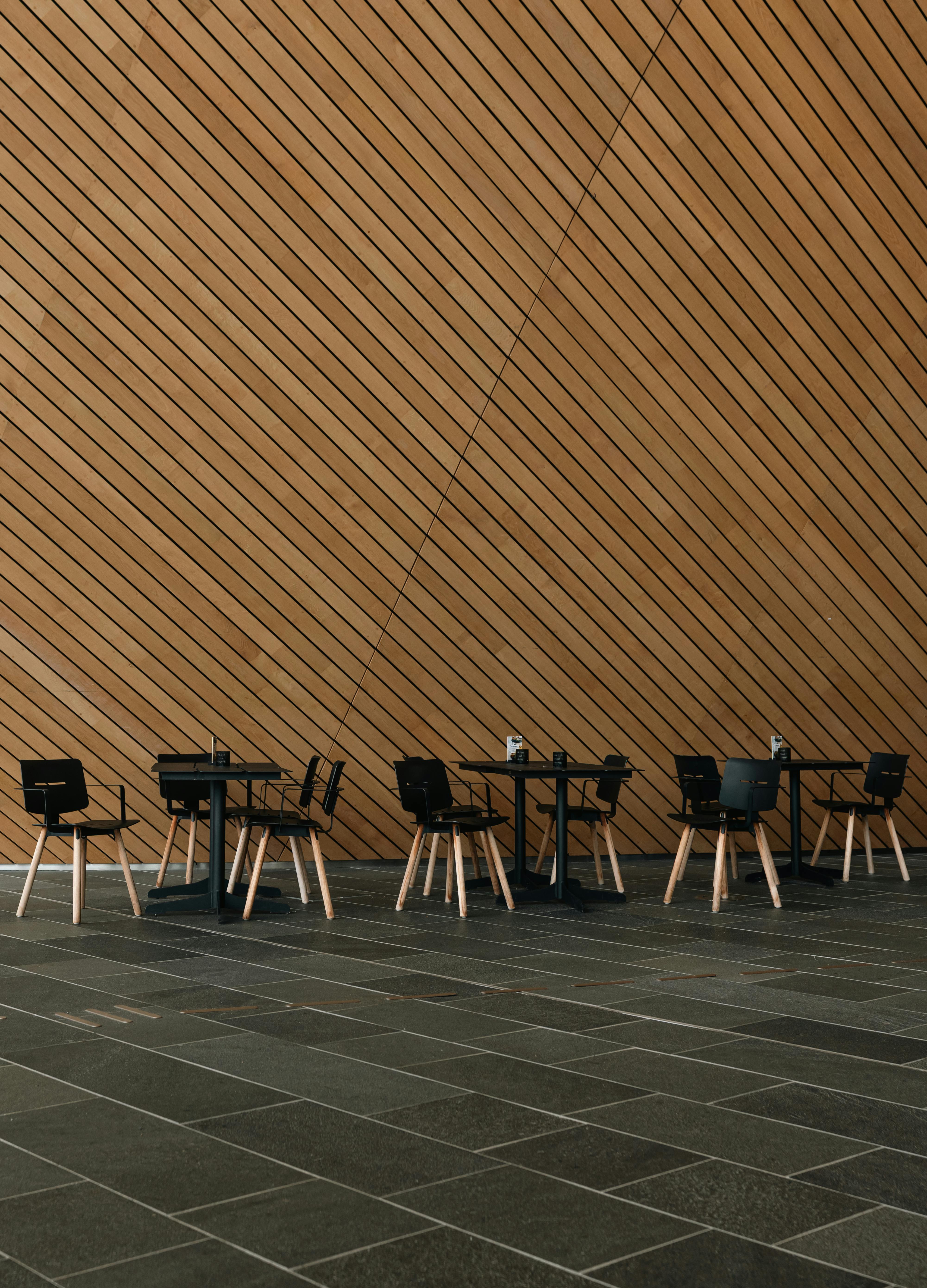 Kostenlos Ein modernes Café mit schwarzen Stühlen und Holztischen vor einer holzgetäfelten Wand. Stock-Foto