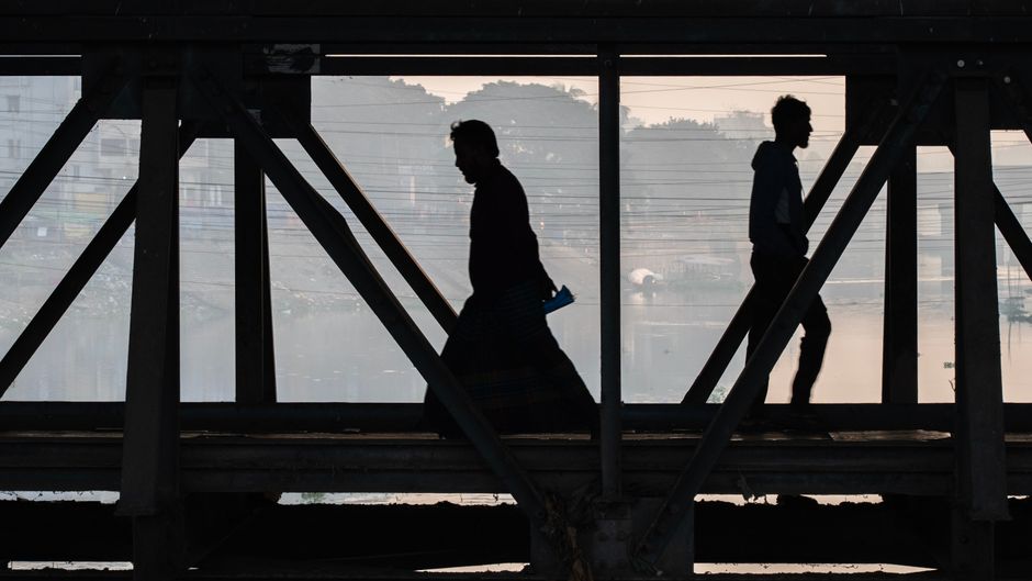 Silhouettes of two people crossing an industrial bridge at dawn, reflecting calm urban life.