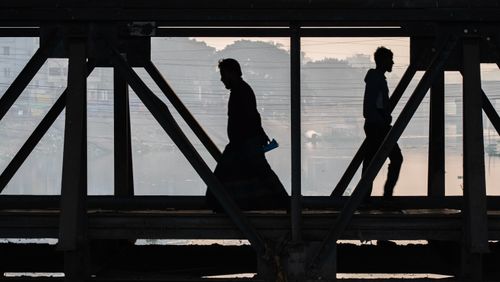 Free Silhouettes of two people crossing an industrial bridge at dawn, reflecting calm urban life. Stock Photo