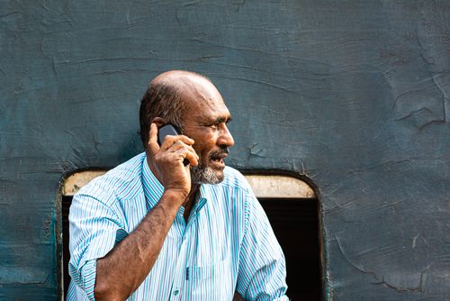 Free An elderly man uses a cellphone while seated by a train window. Stock Photo