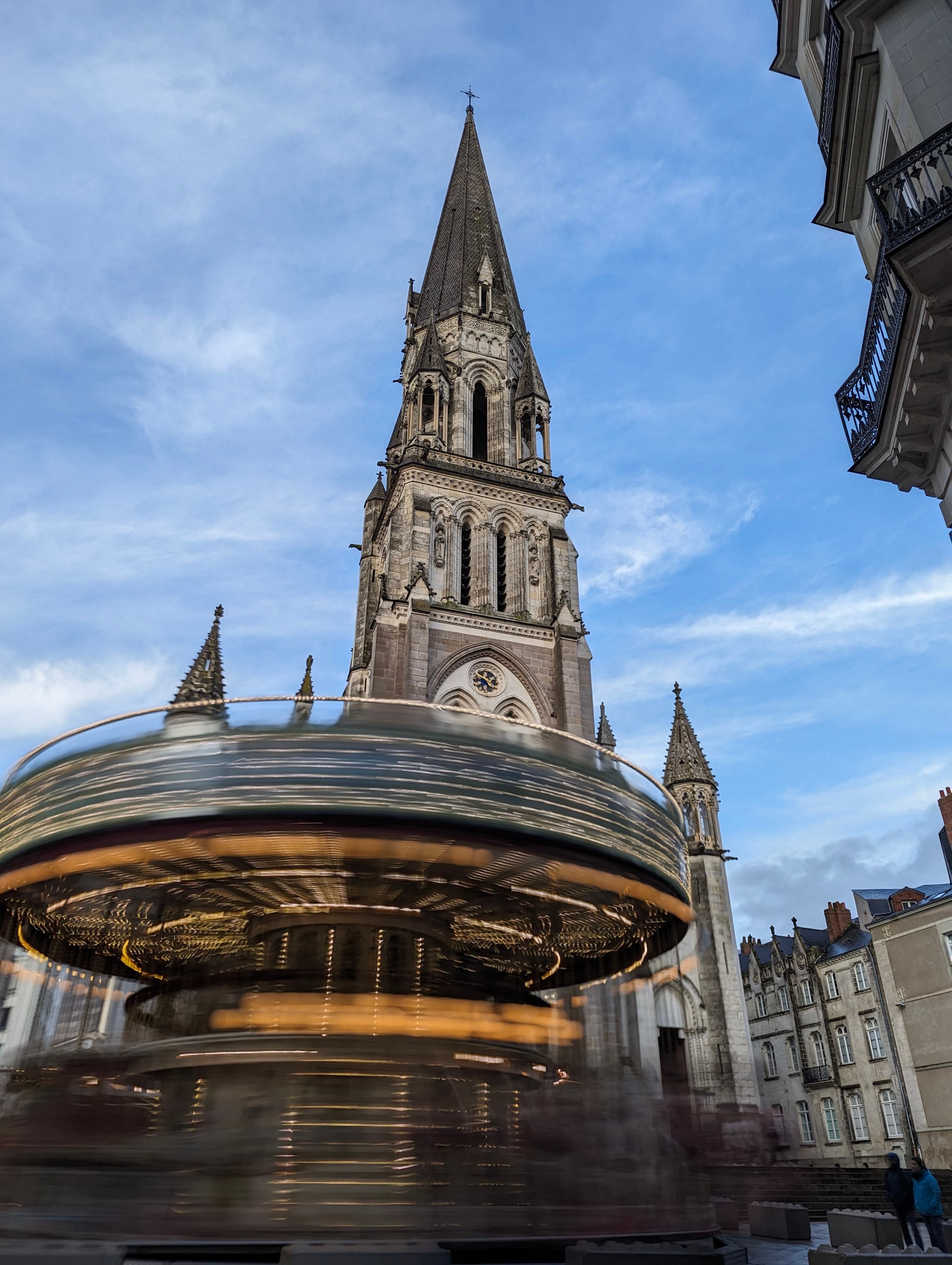 Blurry carousel in motion against the majestic Basilica of Saint Nicolas in Nantes, France.