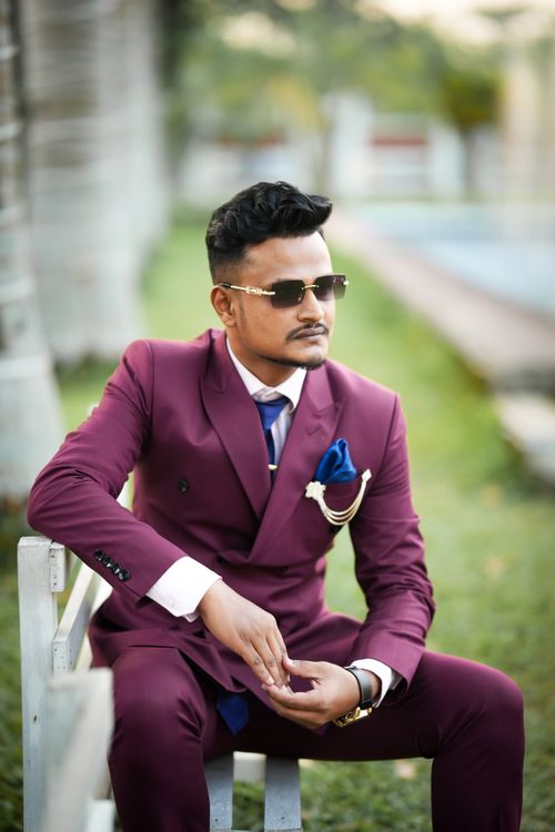 Free A fashionable man in a maroon suit sits outdoors, exuding style and confidence. Stock Photo