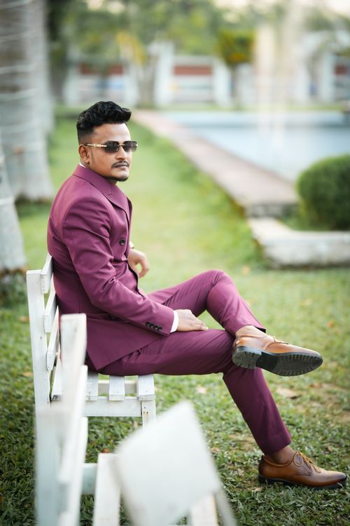 Free Man in purple suit sitting on a bench outdoors in a park setting. Stock Photo