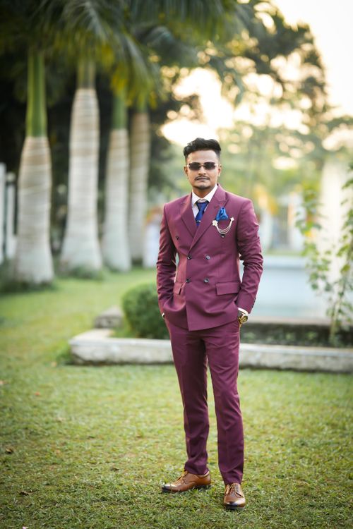 Free Stylish young man in a maroon suit standing outdoors in a garden setting. Perfect for fashion and lifestyle themes. Stock Photo