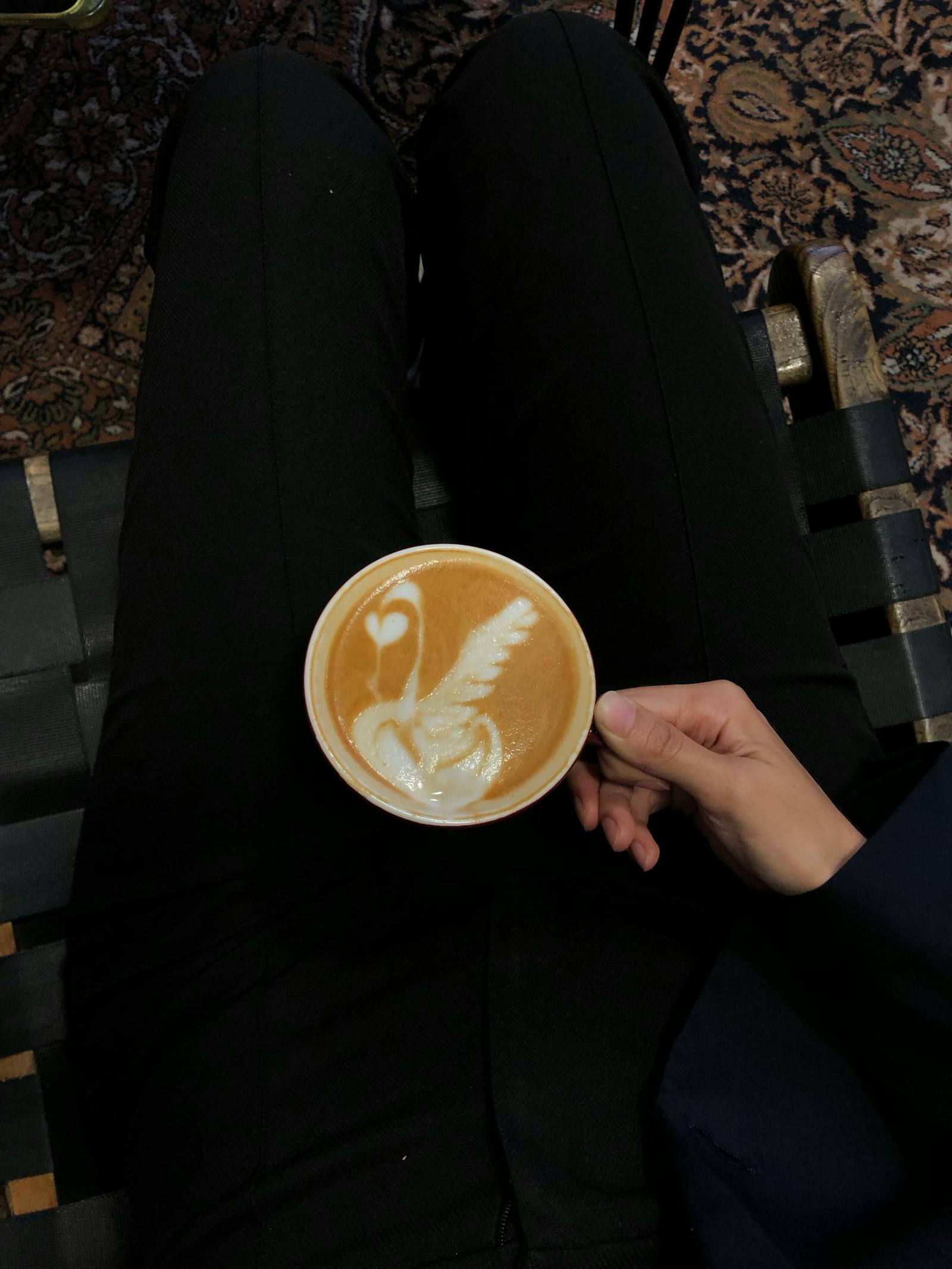 Hand holding latte with swan art in cozy café