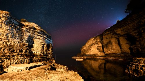 Free Captivating night sky with stars over illuminated rocky cliffs reflecting in calm sea waters. Stock Photo