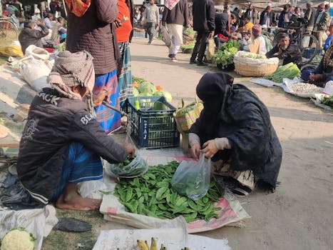 A bustling outdoor market scene with people purchasing fresh vegetables during the day.