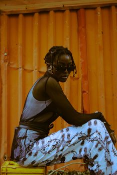 Stylish woman with sunglasses sitting in front of an orange corrugated wall.