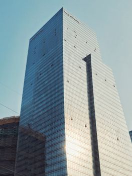 A tall glass skyscraper reflecting sunlight in a bustling urban area.