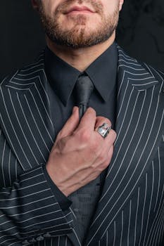 Close-up of a stylish man adjusting his tie, wearing a pinstripe suit and silver ring.