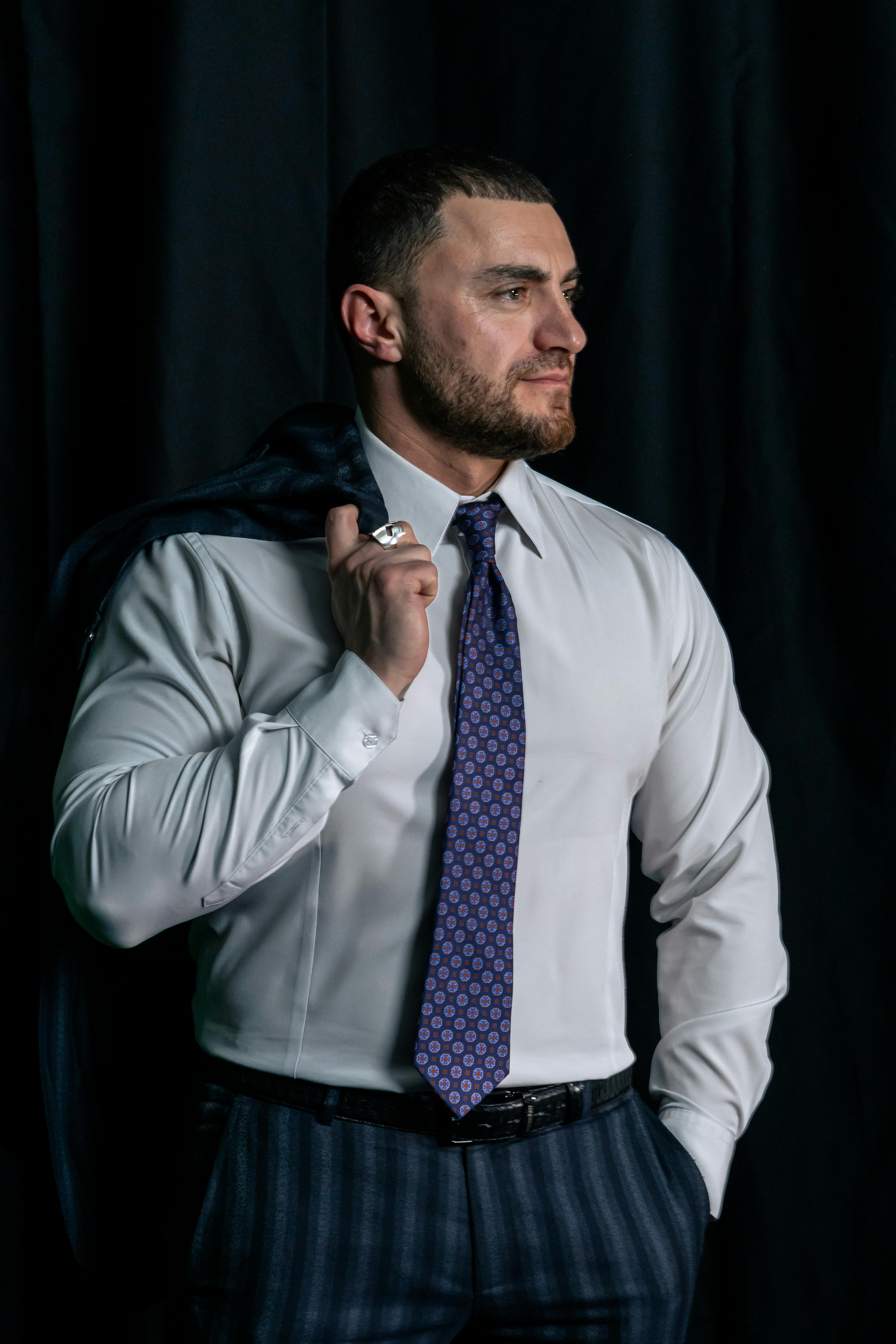 Ilmainen Muotokuva itsevarmasta liikemiehestä muodollisessa puvussa ja solmiossa seisomassa tummaa taustaa vasten. Kuvapankkikuva