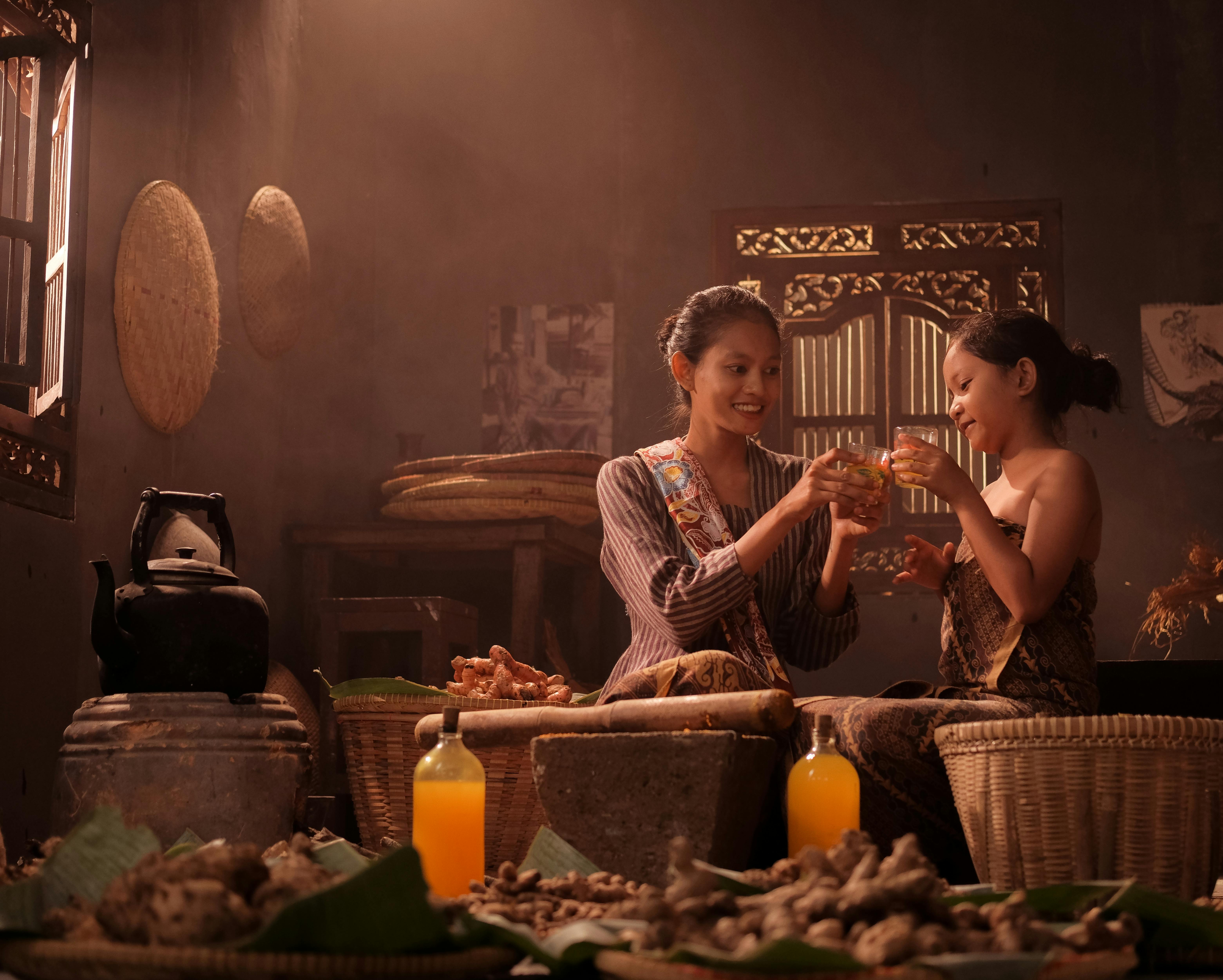 Kostenlos Zwei Frauen in traditioneller Kleidung genießen Getränke in gemütlicher Marktatmosphäre mit Körben und Gewürzen. Stock-Foto