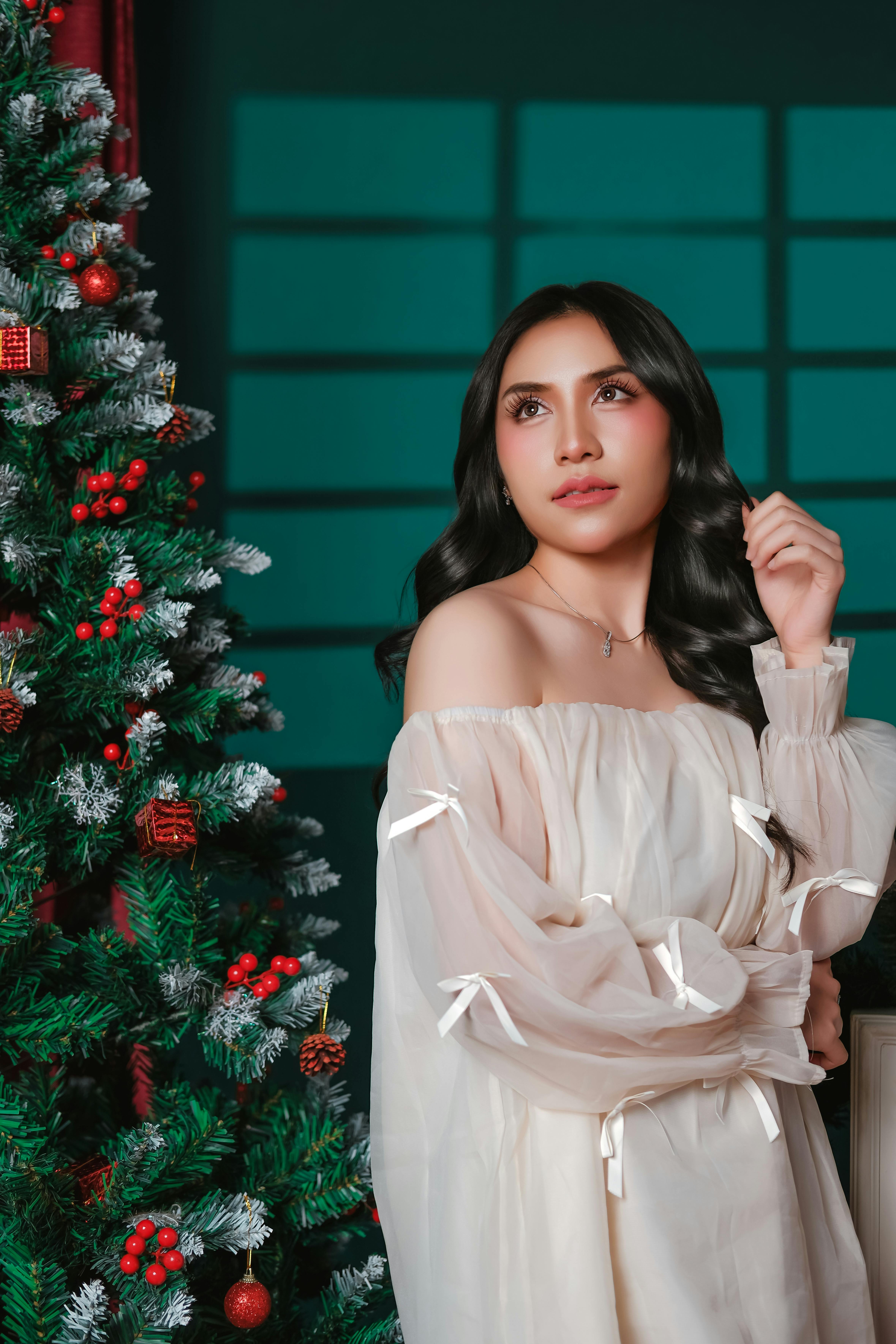 Kostenlos Frau in elegantem Kleid posiert neben einem geschmückten Weihnachtsbaum in einem Innenraum Stock-Foto