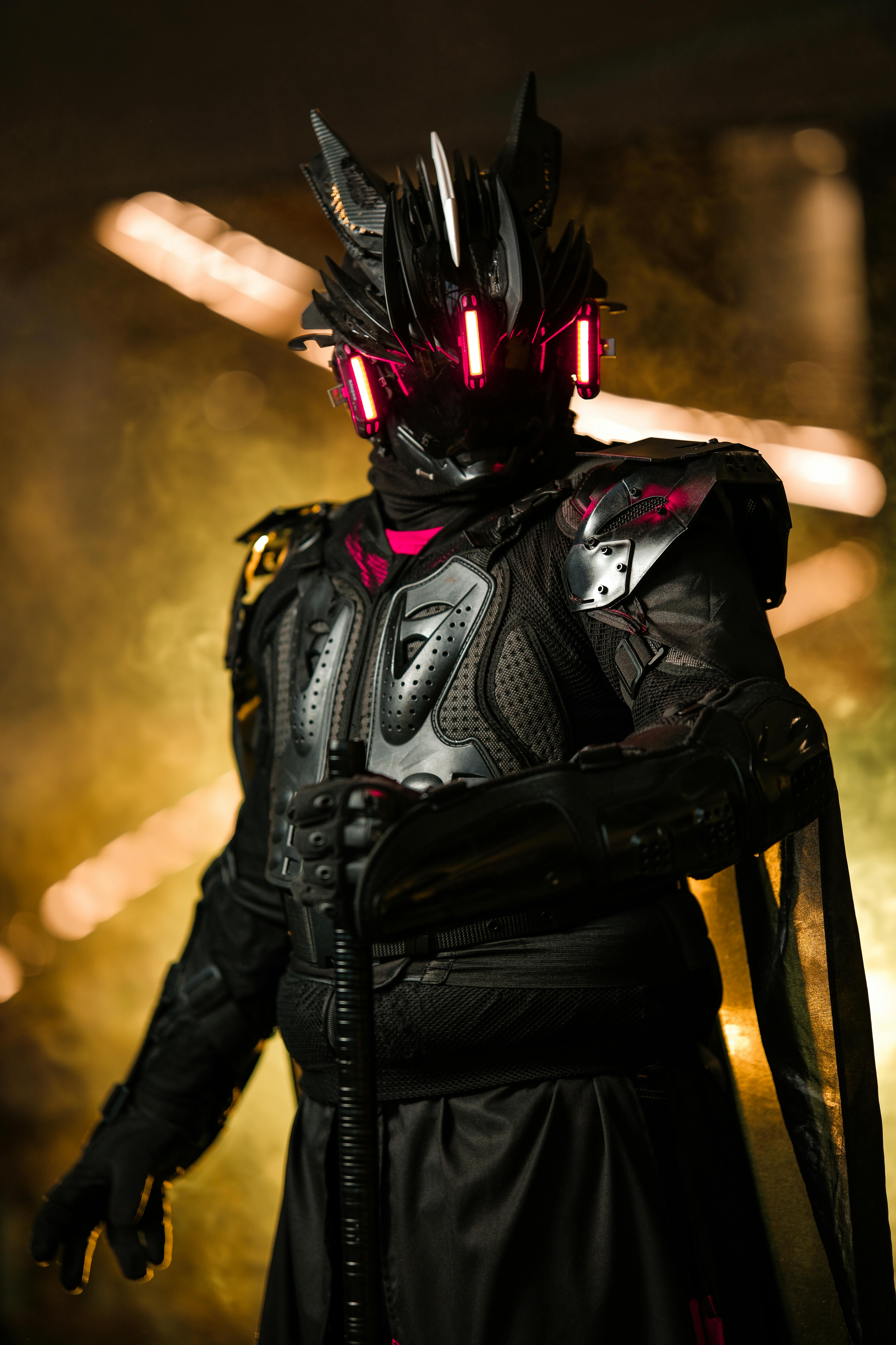 Kostenlos Ein futuristischer Krieger in dunkler Rüstung mit Neonakzenten steht vor einem dramatischen Hintergrund. Stock-Foto