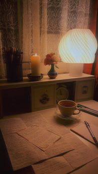 A warm, inviting desk scene with tea, notes, and soft lighting from a lamp and candle.