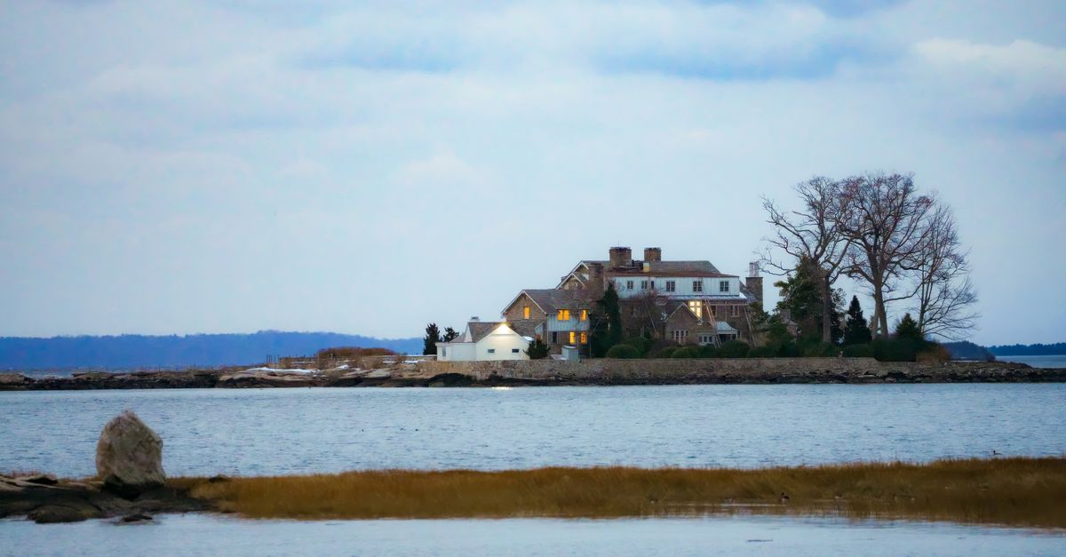 A tranquil view of a mansion on an island surrounded by calm waters.