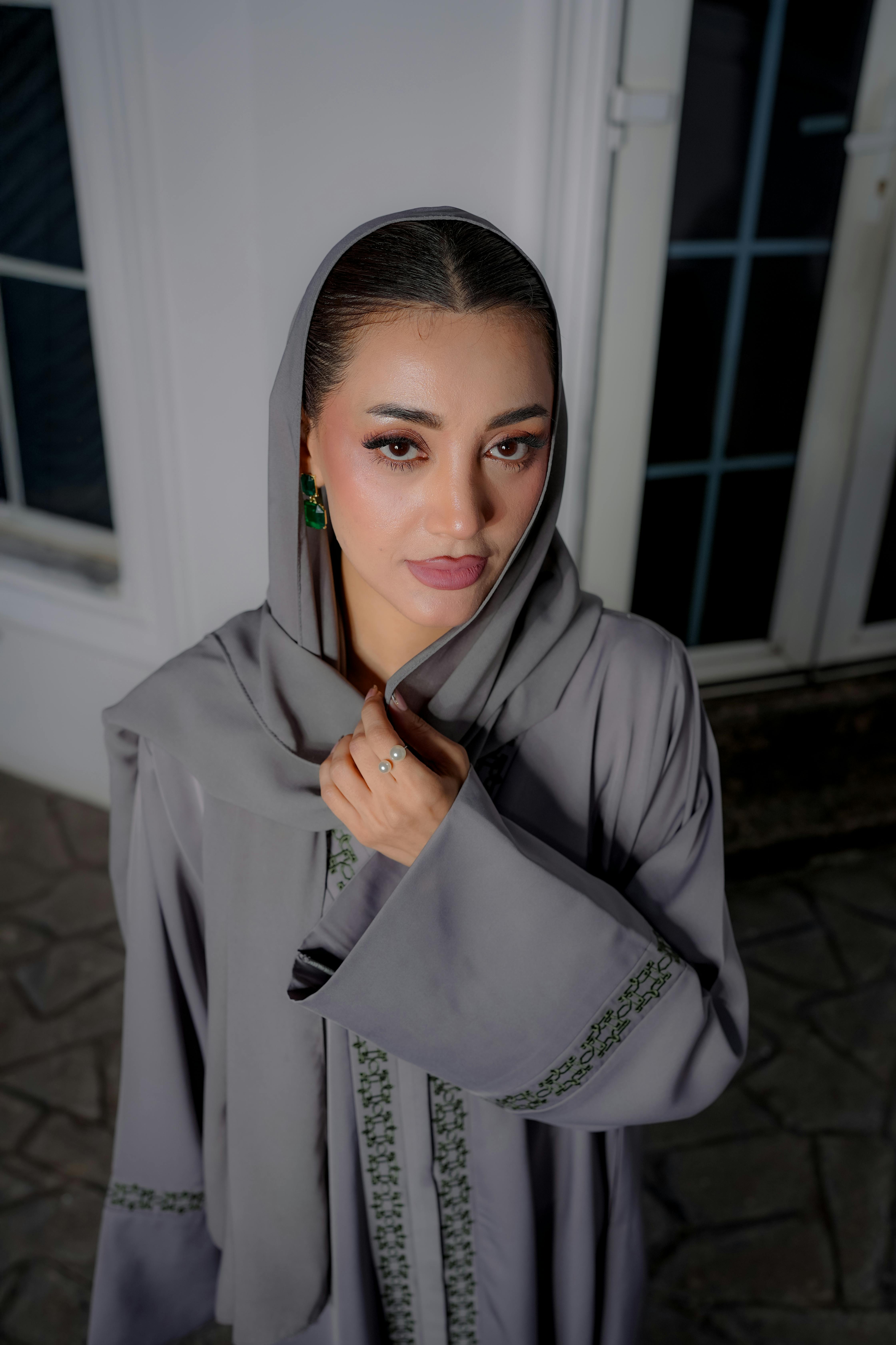 Gratis Mujer con un vestido tradicional gris y pañuelo en la cabeza, de pie en el interior, mirando hacia arriba. Foto de stock