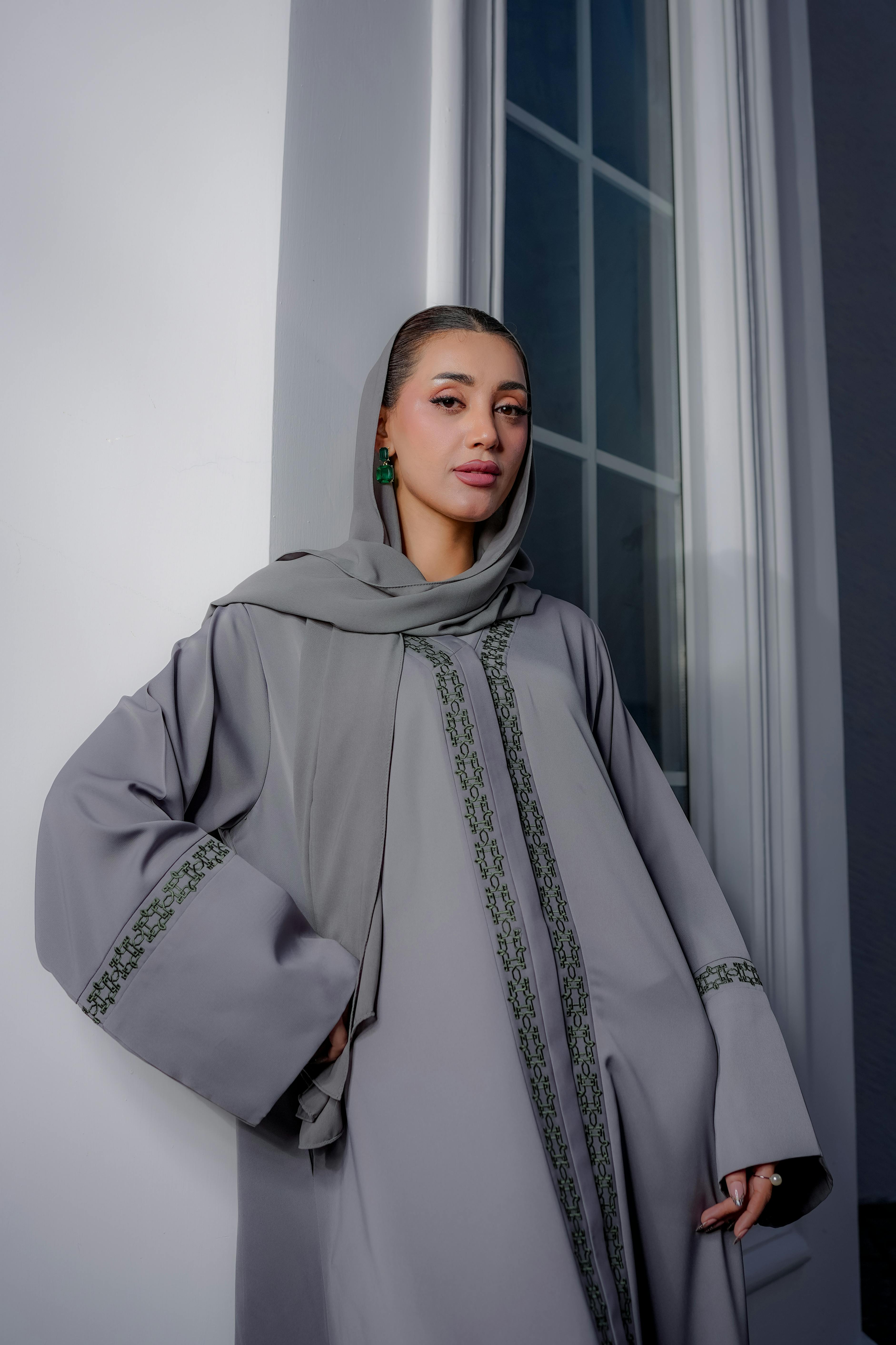 Gratis Retrato de una mujer con una abaya gris junto a una ventana, exudando elegancia. Foto de stock