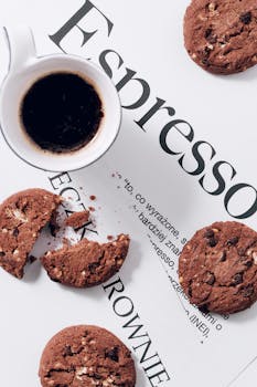 Stylish flat lay of espresso with chocolate chip cookies on printed paper. Perfect for coffee lovers.