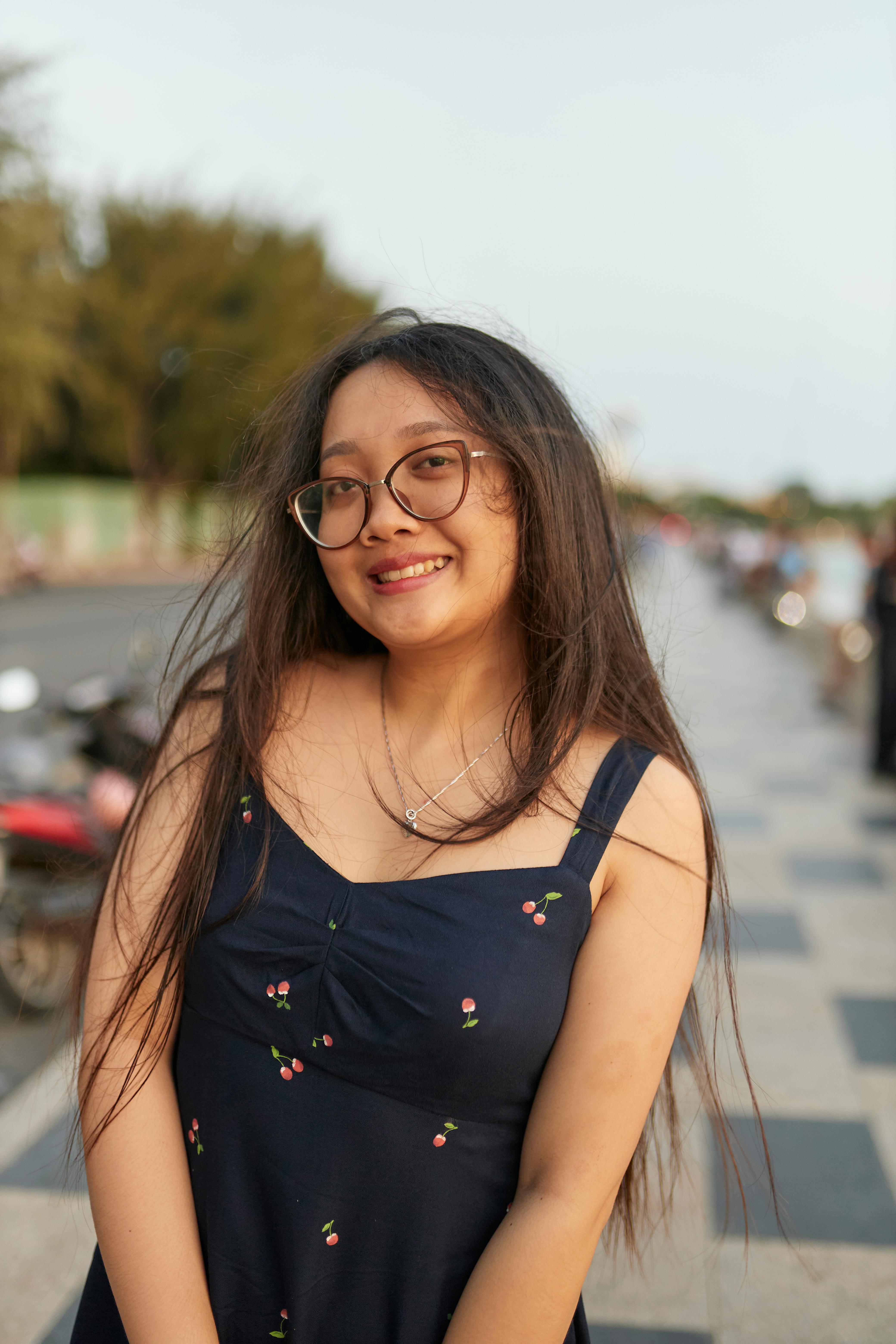 Kostenlos Junge Frau mit langen Haaren und Brille lächelt im Freien in Vũng Tàu, Vietnam. Stock-Foto