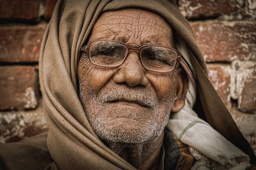 Free Close-up portrait of an elderly man wearing glasses and traditional attire against a brick wall. Stock Photo