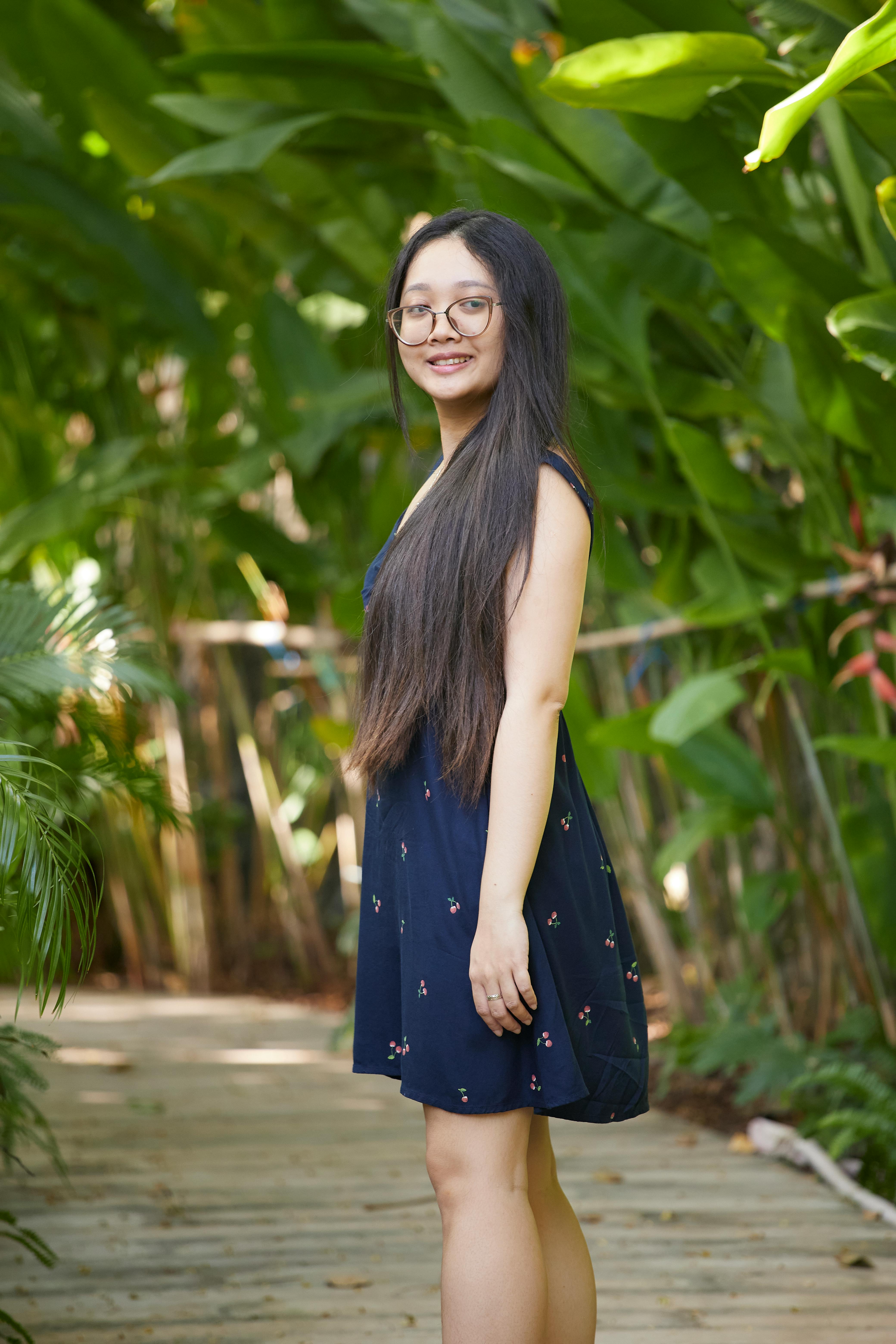 Kostenlos Junge Frau in einem blauen Kleid steht auf einem Holzsteg, umgeben von üppigem Grün in Vietnam. Stock-Foto